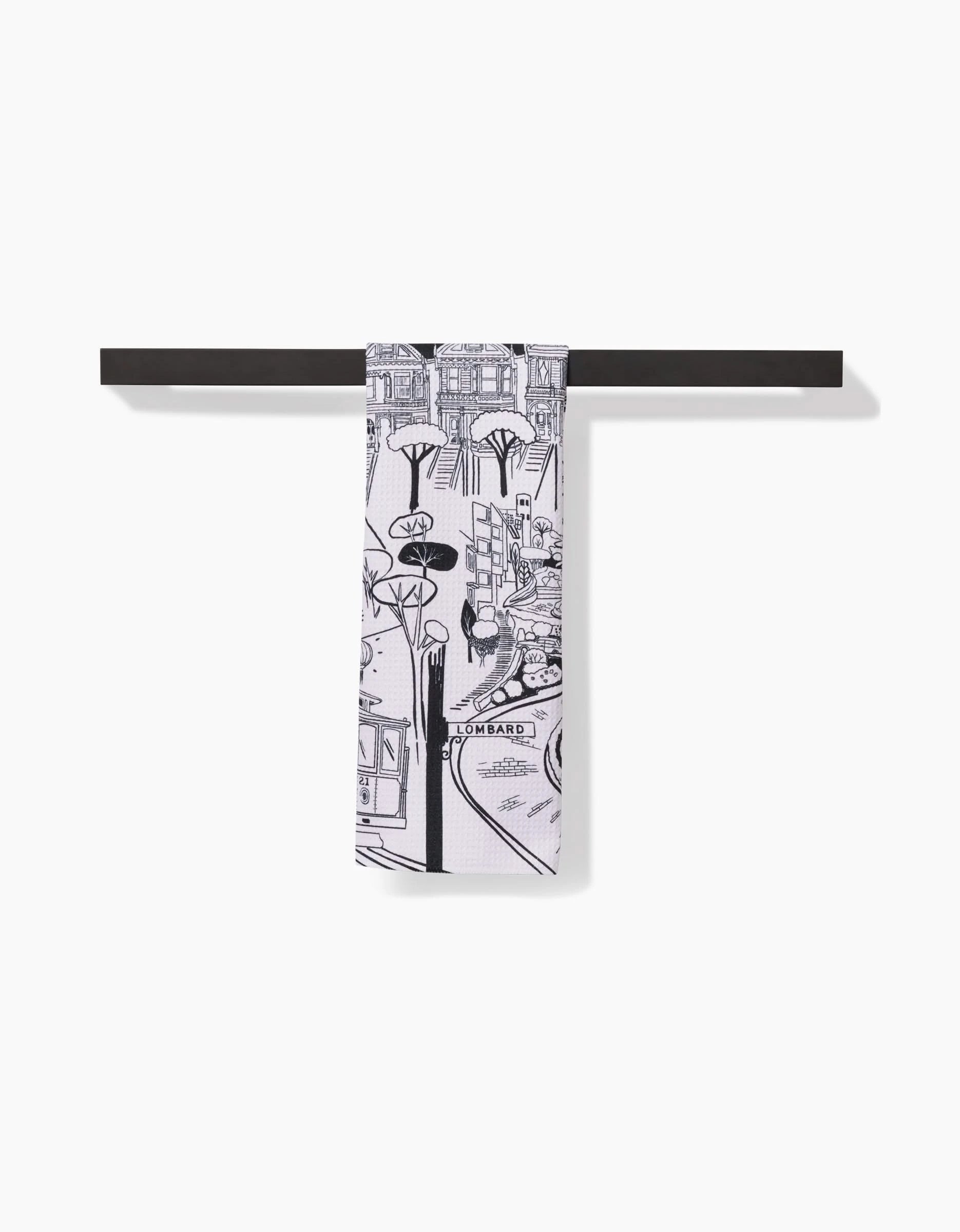 The Elisabeth Wing San Francisco Tea Towel, made with absorbent Geoweave fabric and featuring a black-and-white cityscape, hangs neatly over a dark towel bar against a white background.