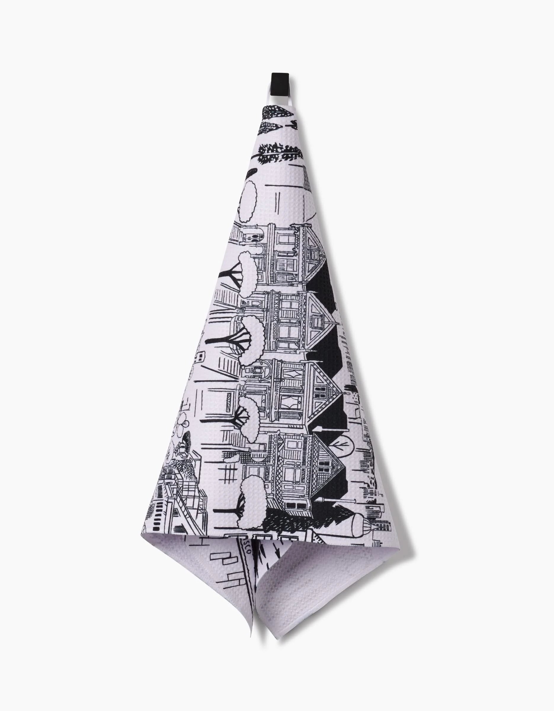 A San Francisco tea towel by Elisabeth Wing, made from Geoweave fabric, features black Victorian-style houses and snowy scenes on white and hangs from a black loop.