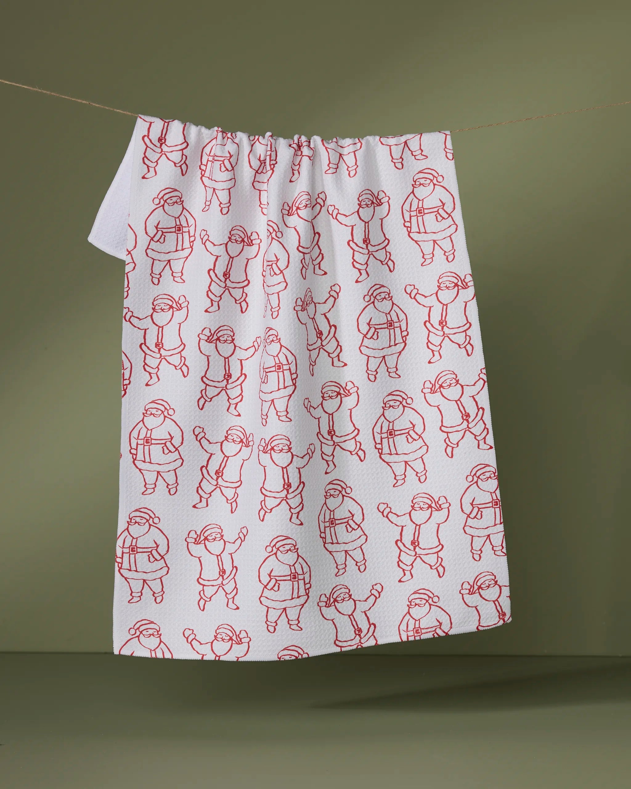 The Geometry "Santa Groove" tea towel features red line drawings of playful children on white fabric, hanging against an olive green background—a charming and practical recycled kitchen towel.