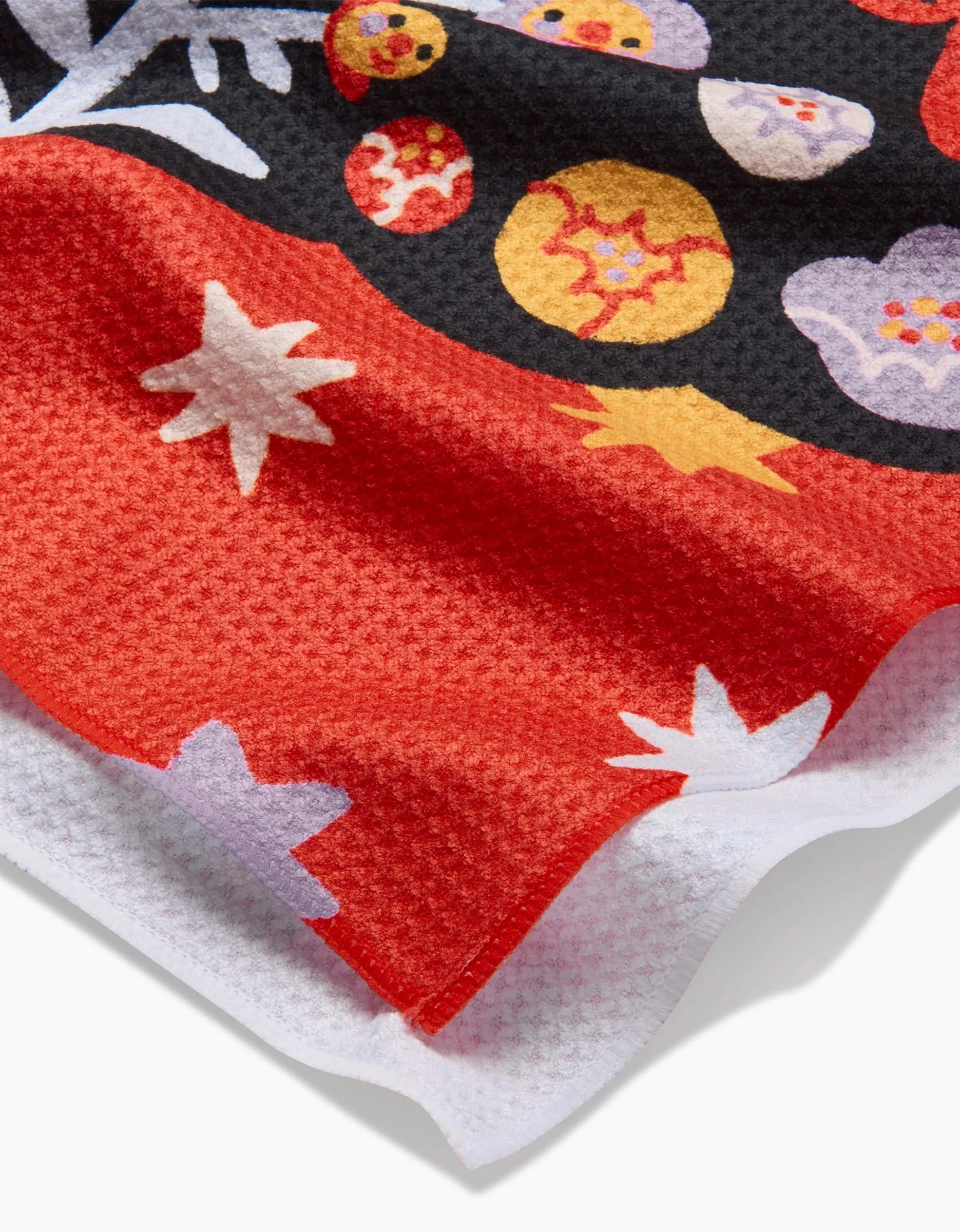 The So Lazo Santa Muerte tea towel features textured red, black, and white fabric with vibrant floral and abstract patterns, visible woven details, and gently curved edges.