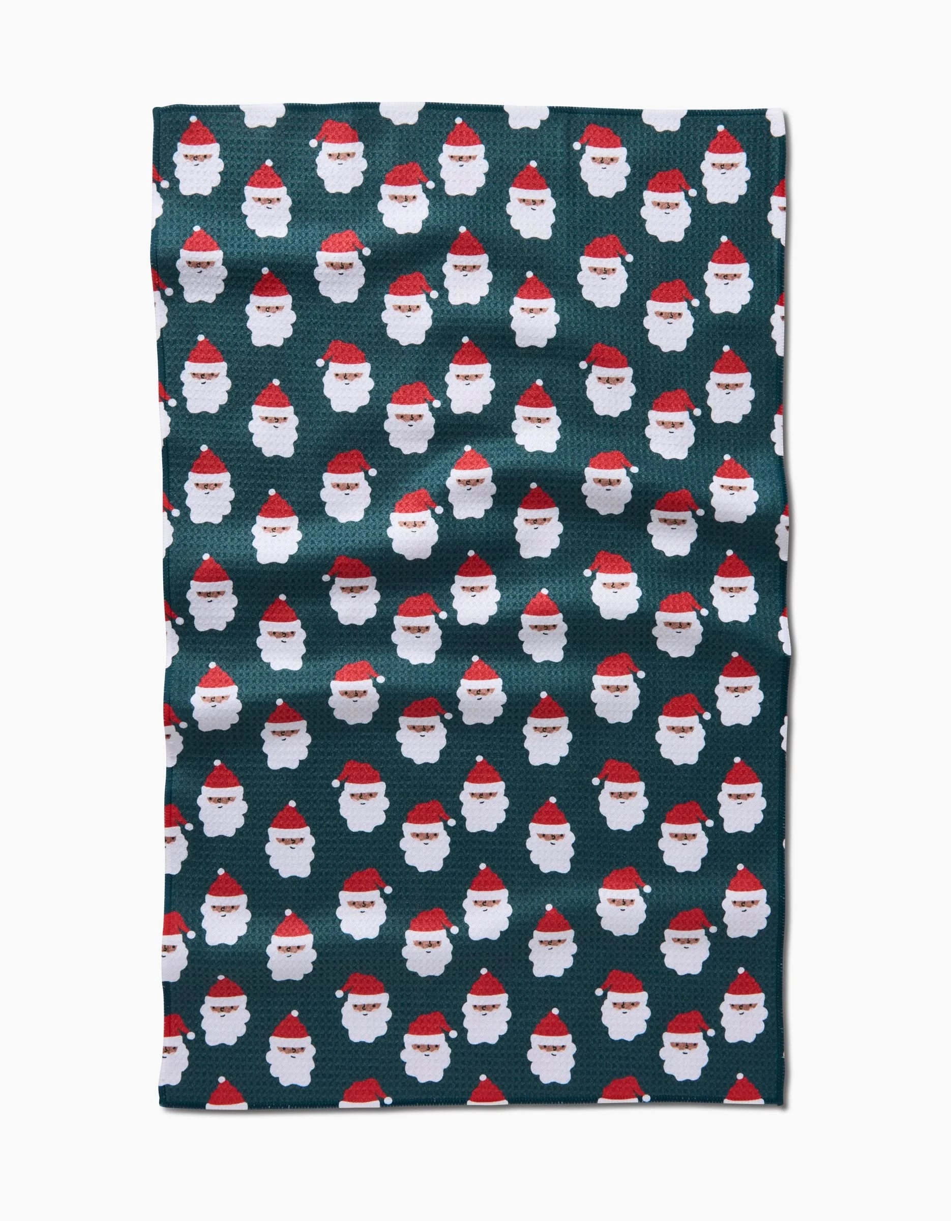 The Santa Santa kitchen towel by Charlie Rowan Designs features a dark green color, is made from recycled materials, and displays rows of white Santa Claus faces in red hats patterned evenly across the surface.