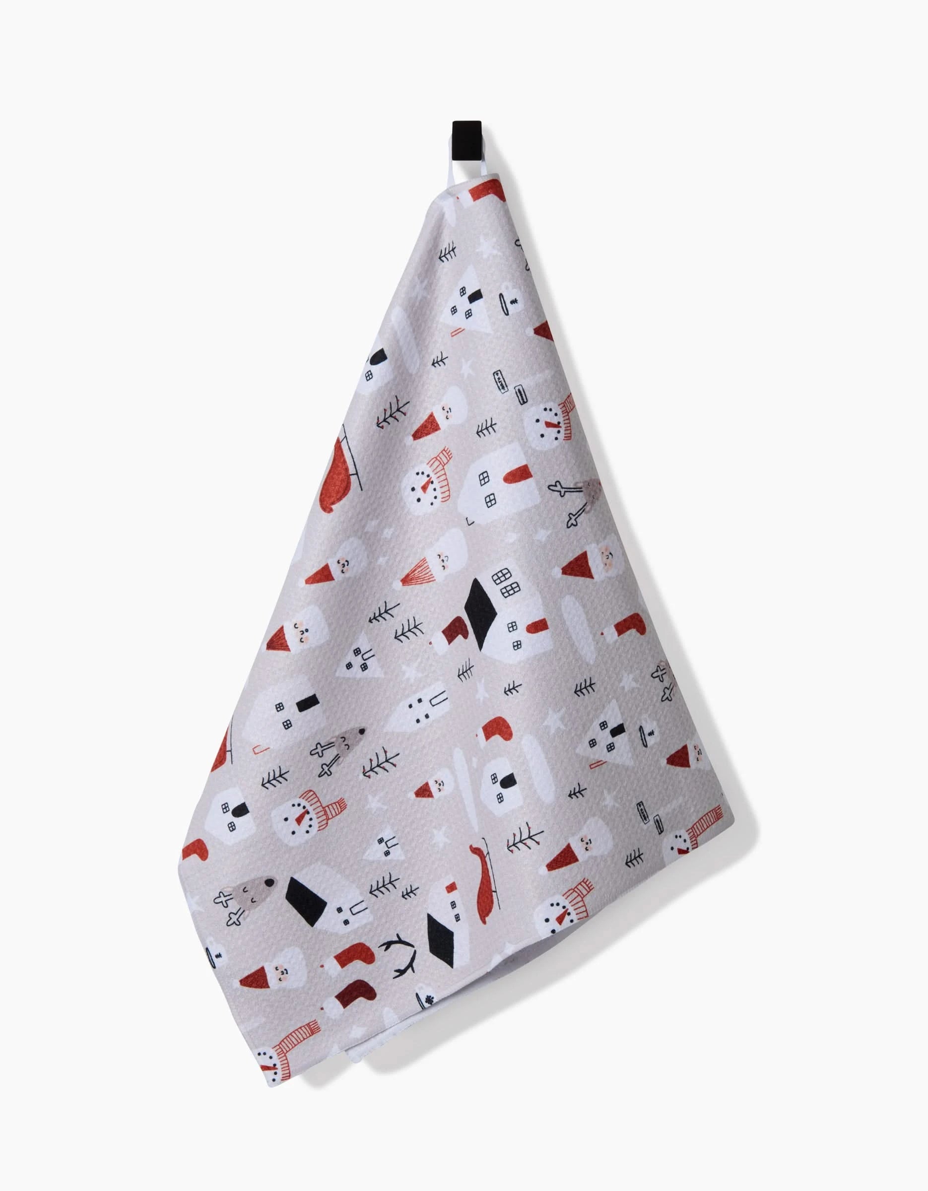 The Santas Village tea towel by Coit Creative features a festive white design with snowmen, trees, snowflakes, and red accents. It hangs from a black loop against a plain white background.
