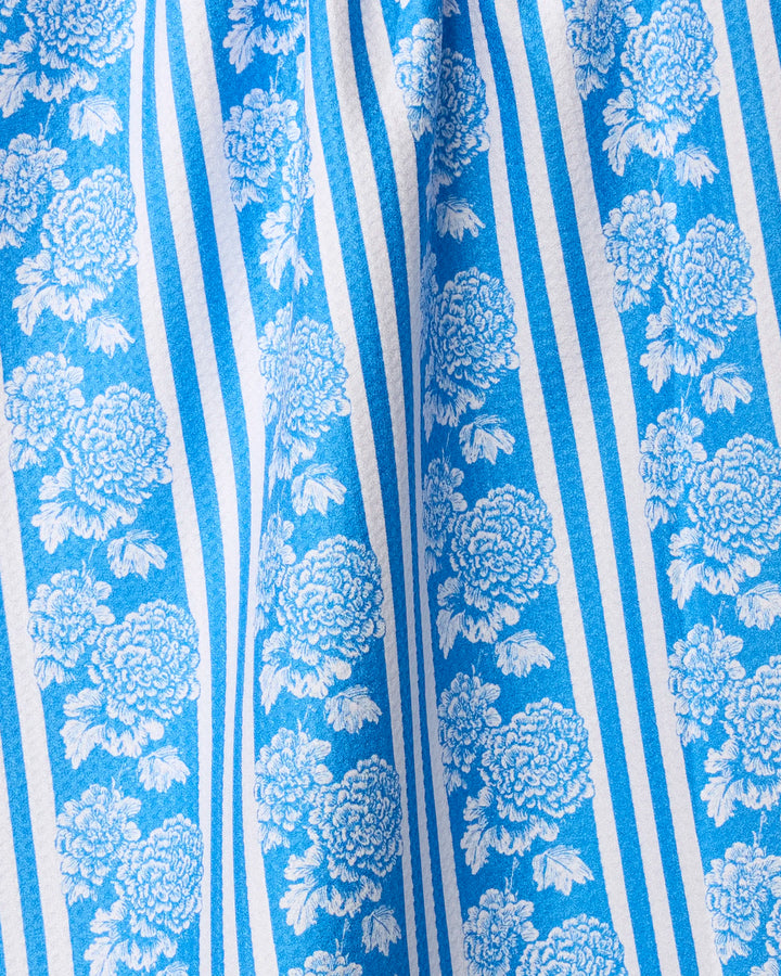 The Geometry Santorini towel features blue and white vertical stripes with a large floral pattern. Ultra-absorbent and gently gathered for soft folds, it combines functional elegance with striking design.