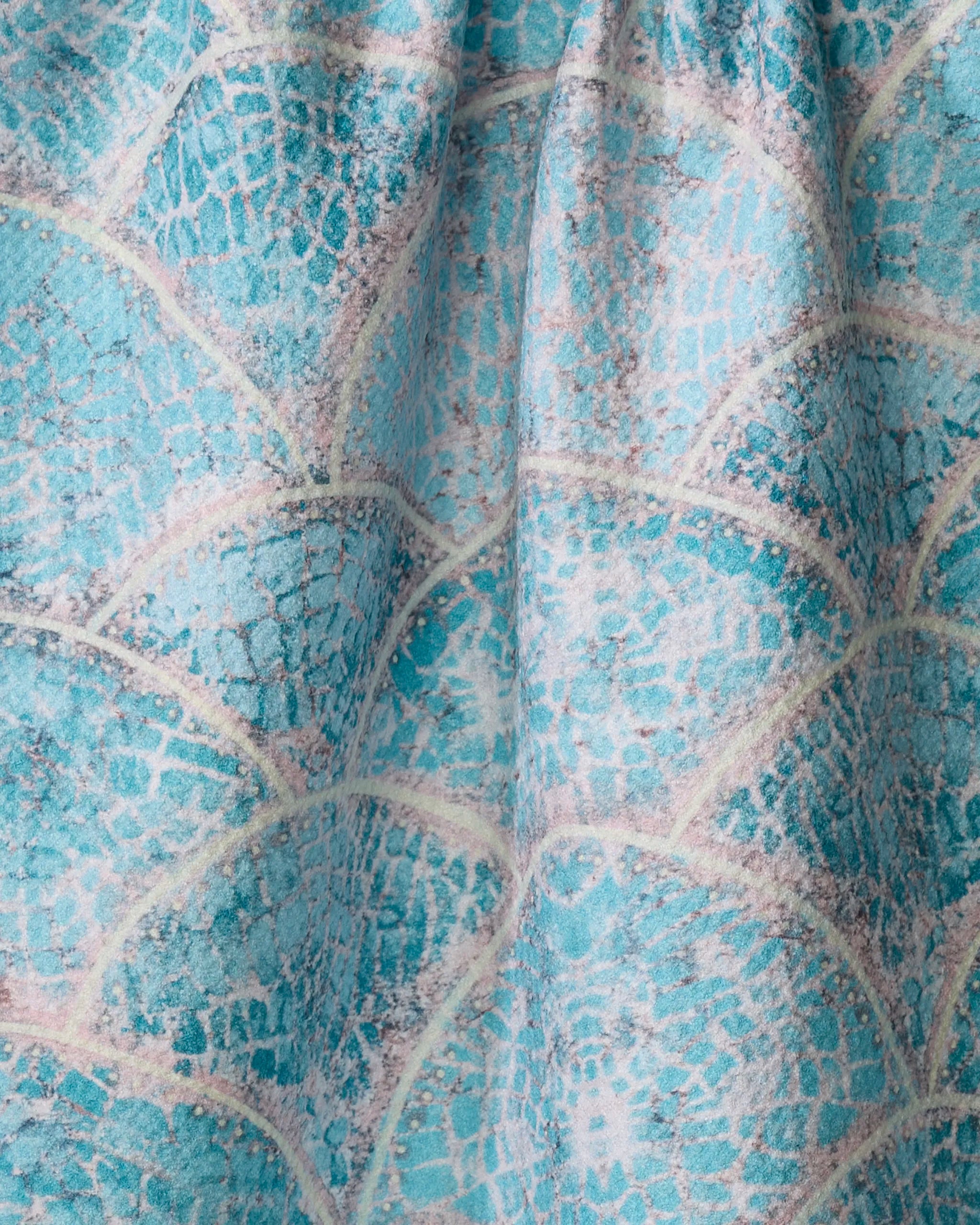Close-up of the Scallop Hills tea towel by Taryn Brennan, showcasing its turquoise and white scale-like design with textured folds and soft fabric shadows.