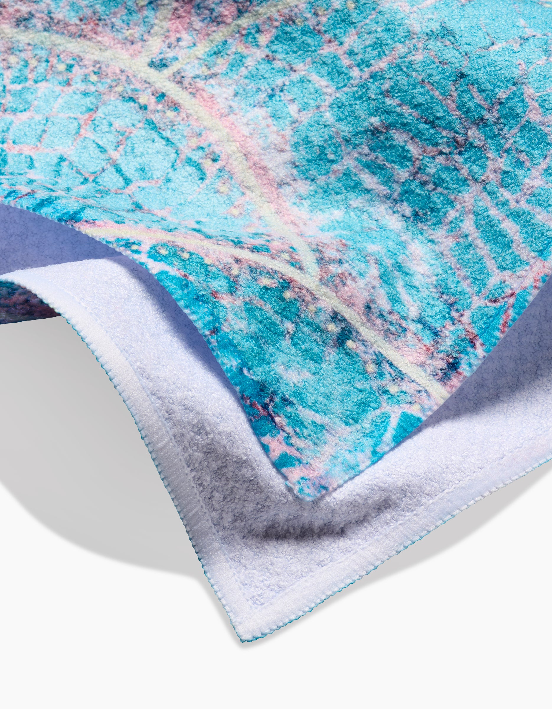 Close-up of the Taryn Brennan “Scallop Hills” tea towel, showing its vibrant blue, teal, and pink abstract pattern on one side and plain white on the other. Features edge stitching and a texture made from ultra-absorbent recycled materials.
