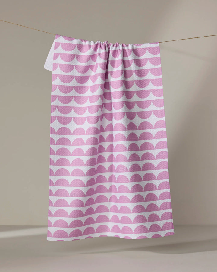 The Buy Guide's "Scallops - Pink" eco-friendly dish towel features a pink and white repeating scallop pattern, shown hanging against a neutral background.