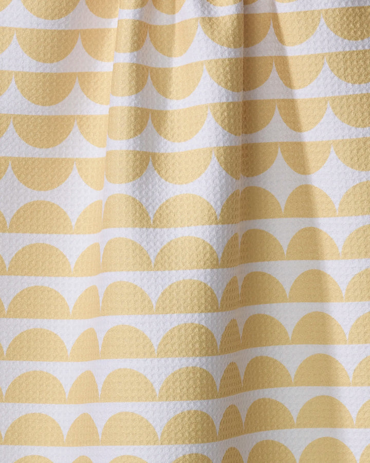 A close-up of The Buy Guide’s Scallops - Yellow tea towel shows its white, textured surface with a repeating pattern of yellow semi-circles and lines in a geometric, scalloped design.