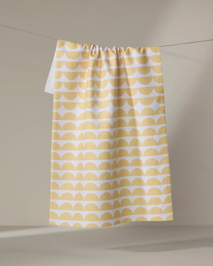 The Buy Guide's Scallops - Yellow tea towel features a yellow and white semicircle pattern and hangs on a string against a neutral backdrop.