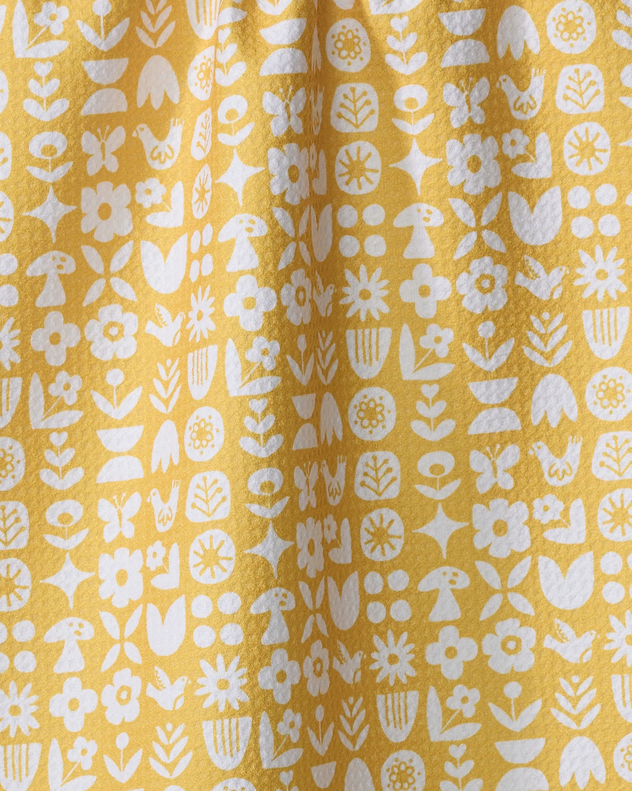 The Kayla Ann Scandi Spring tea towel features a yellow backdrop with white flowers, leaves, and mushrooms in vertical rows. Made from recycled materials, it offers a softly textured, quick-drying fabric with gentle folds.