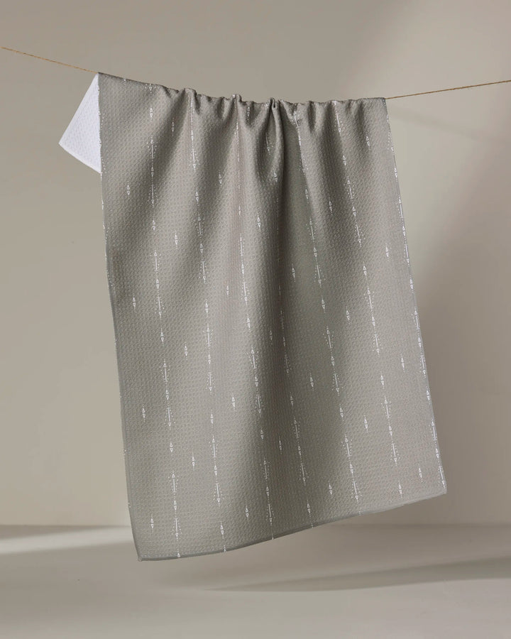 The Hufton Studio Scandi Trails tea towel, featuring a gray textured design with a subtle vertical white pattern and an ultra-absorbent white reverse side, hangs on a clothesline against a neutral background.