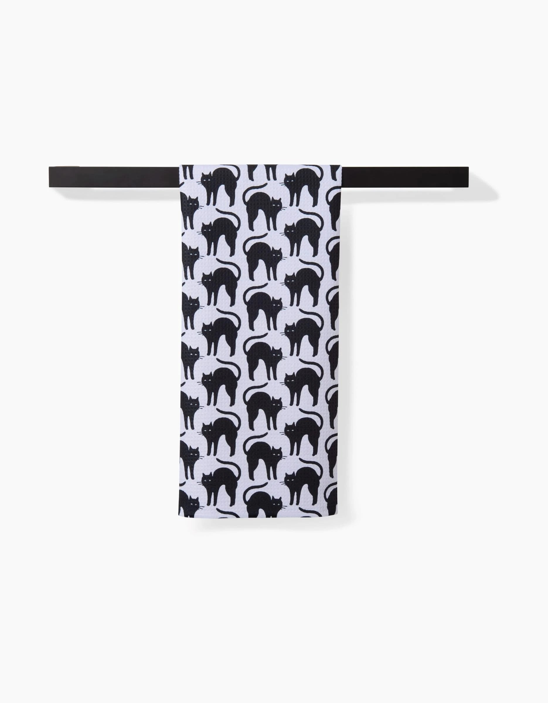 A Hufton Studio Scaredy Cat Black tea towel made from recycled materials hangs on a black rod, featuring a repeating black cat pattern.
