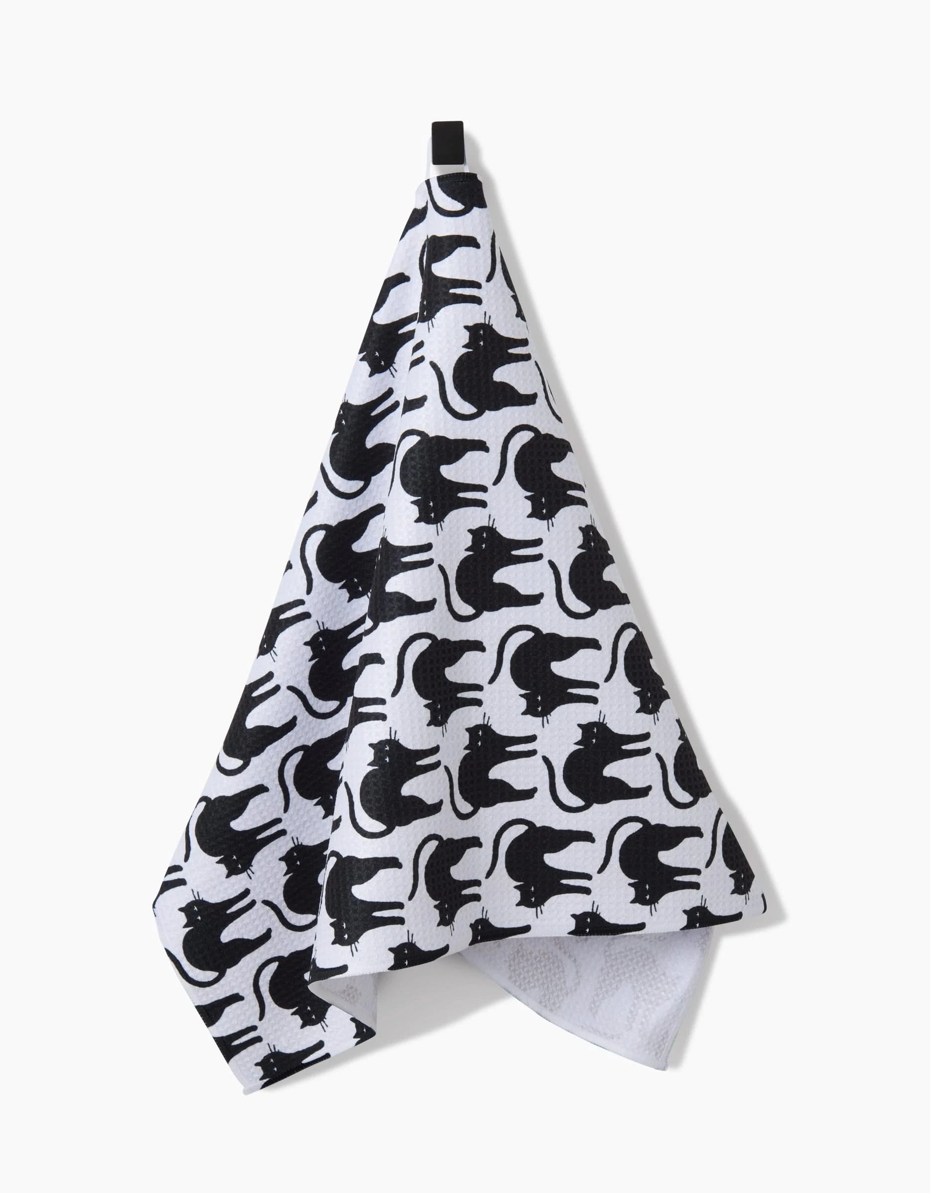 The Scaredy Cat Black tea towel by Hufton Studio, featuring a repeating pattern of black cat silhouettes, hangs from a black hook against a plain white background.