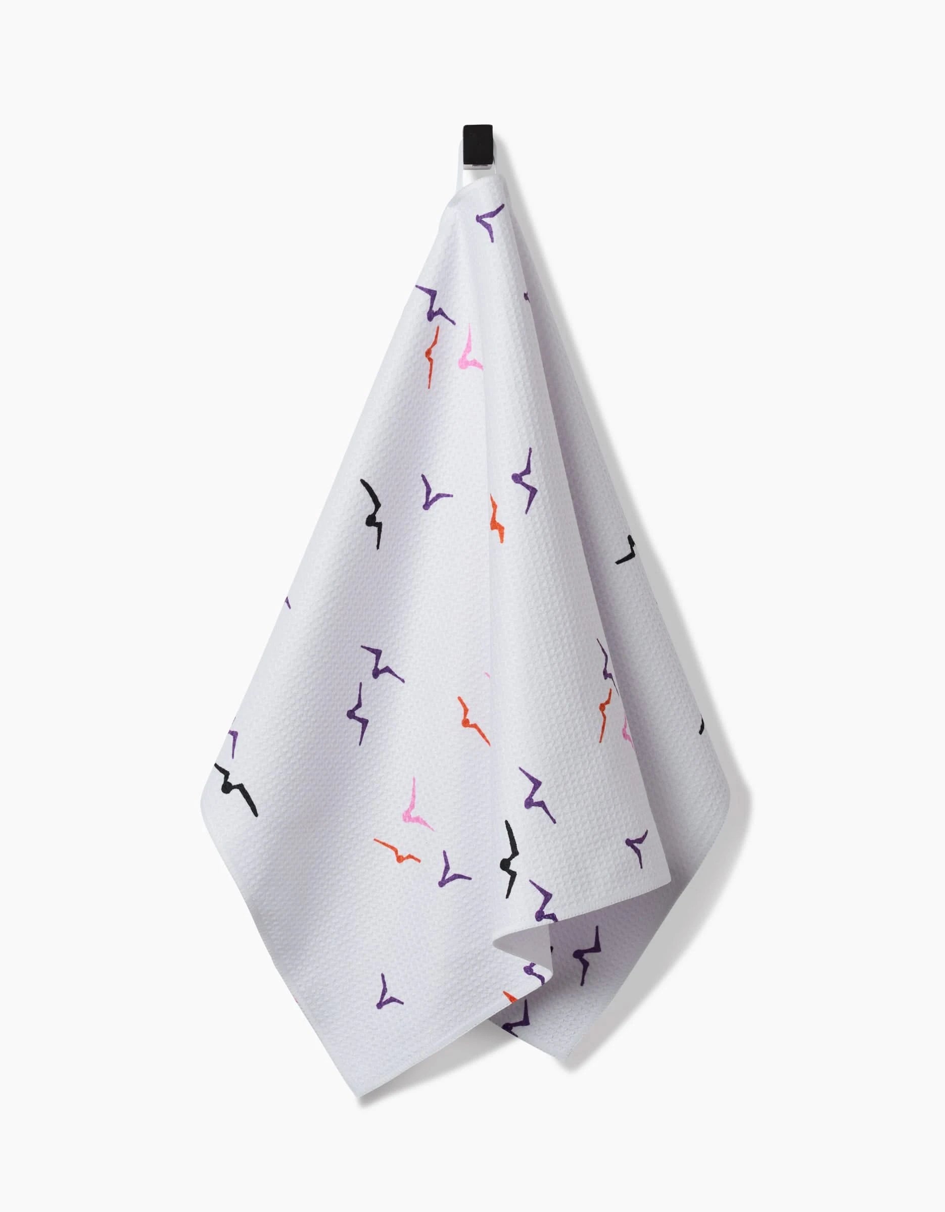 The Scattered Seagulls tea towel by Ania Zwara Art features quick-drying white fabric with a subtle waffle texture and abstract bird shapes in black, purple, pink, and red, hanging from a black loop against a white background.