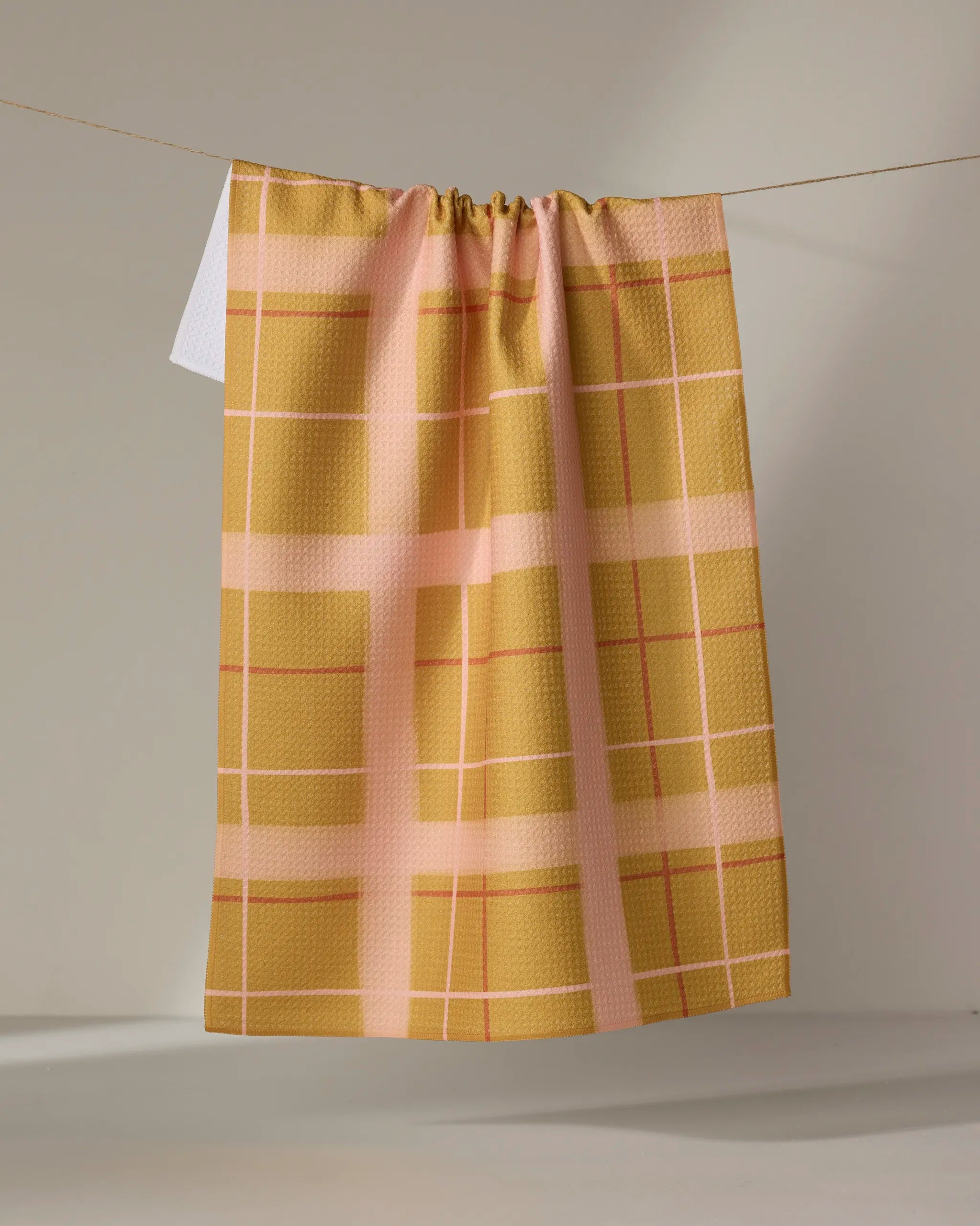 The Elisabeth Wing Scotland Yard tea towel, in absorbent yellow and pink plaid, hangs on a clothesline against a plain light background.