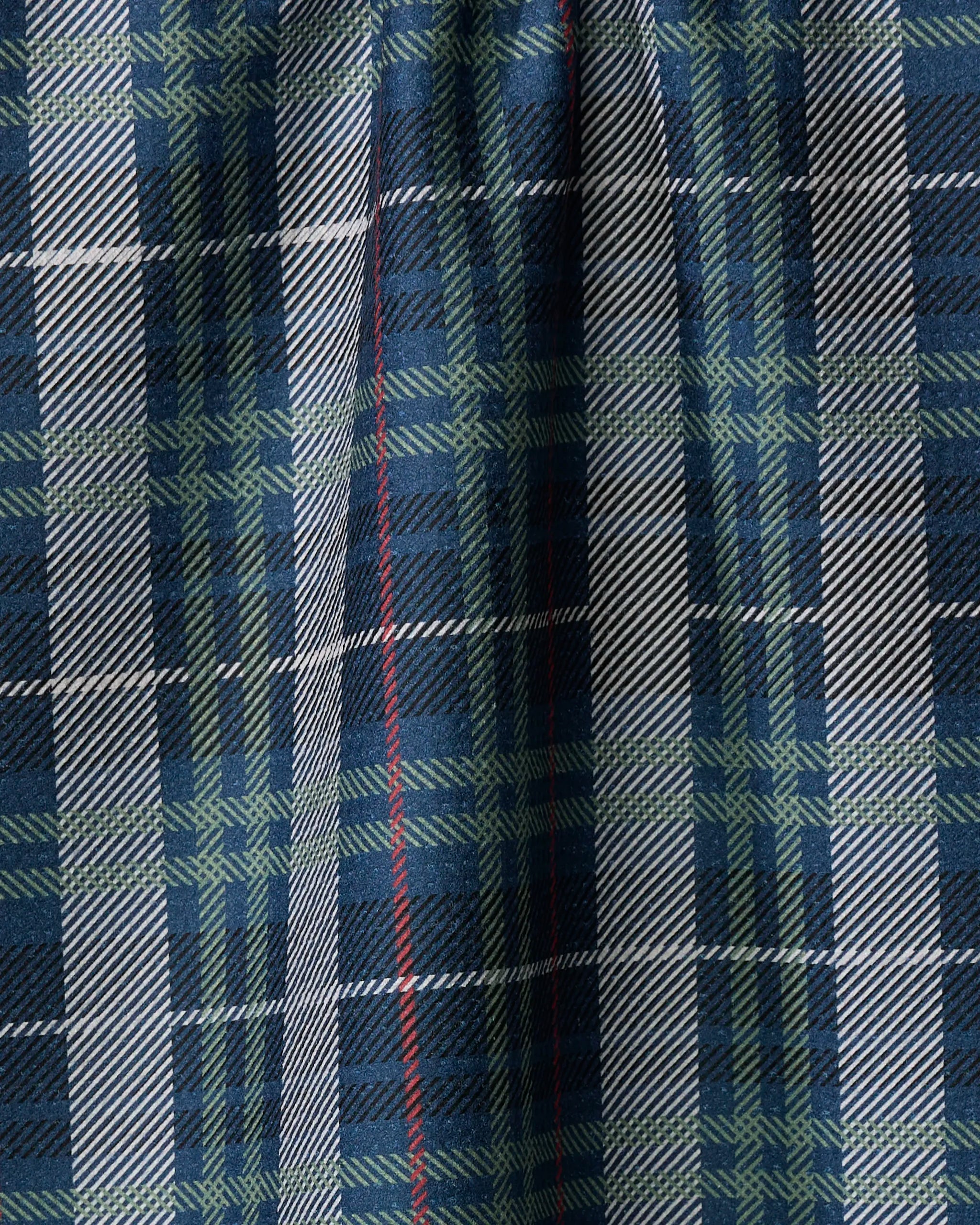 A close-up of Becki Owens' Scotty tea towel, featuring blue, green, black, and white tartan plaid with a thin red vertical stripe. The fabric is shown slightly pleated or draped.