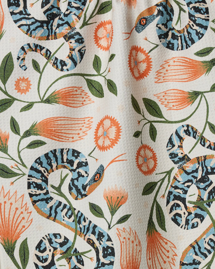Scutes by Geometry features blue and black striped snakes with orange flowers and green leaves on a textured white background—perfect for a recycled or absorbent tea towel to add color to your kitchen.
