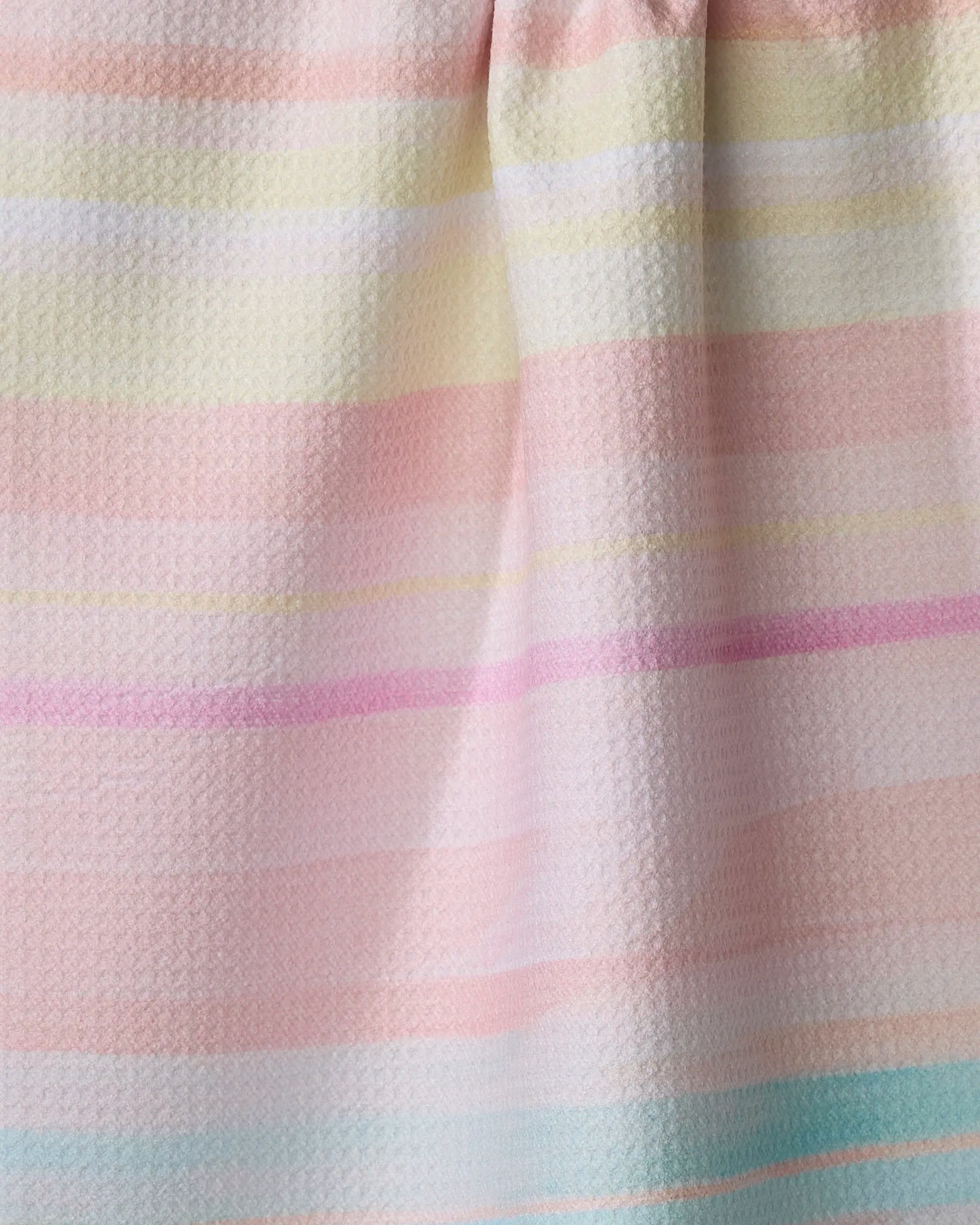 A close-up of the "Seafoam" kitchen tea towel by Stefanie Bales, made from recycled materials with pastel pink, yellow, peach, mint, and white horizontal stripes. The soft woven fabric features gentle folds.