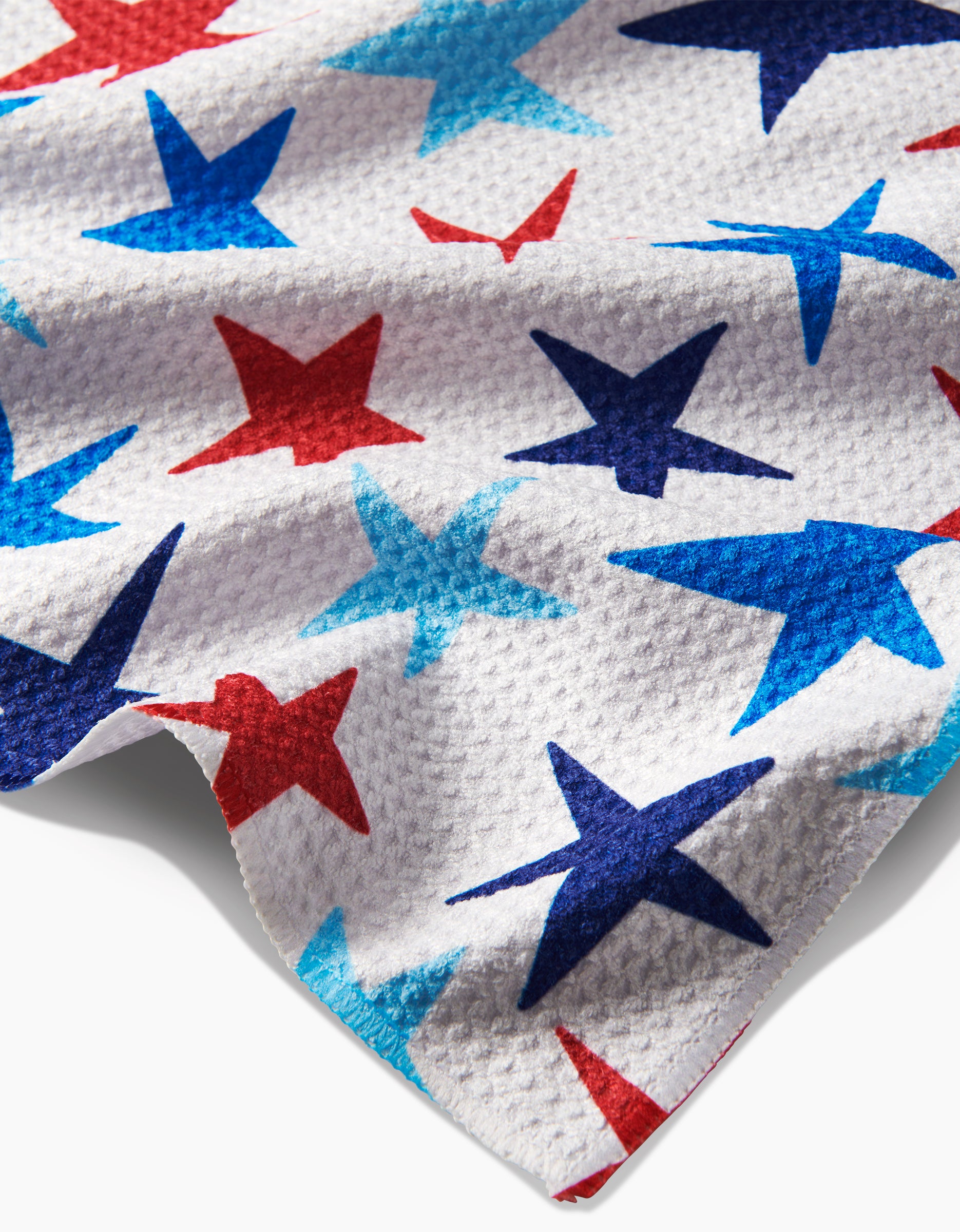 The Mindfulnice “Seeing Stars” Tea Towel features white Geoweave™ fabric with red, blue, and light blue stars in various sizes. The textured material creates soft shadows and highlights for added depth.