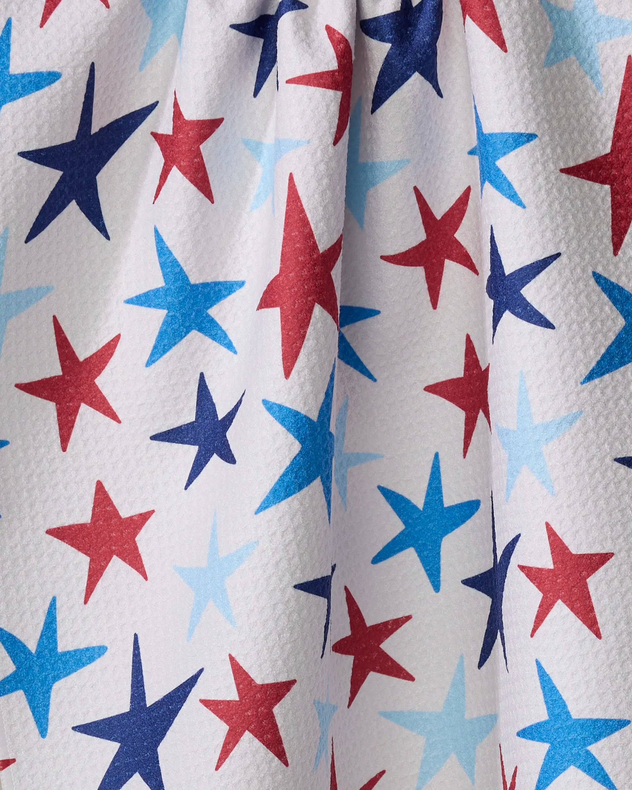 Close-up of Mindfulnice's Seeing Stars tea towel, crafted from recycled materials. White textured fabric features overlapping red and blue stars, with a gathered top creating soft folds and shadows.