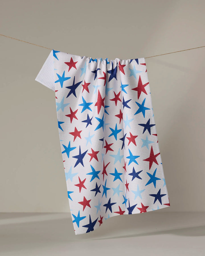 The Mindfulnice "Seeing Stars" towel, ultra-absorbent and white with red, blue, and light blue stars, hangs on a clothesline against a neutral background—ideal as a kitchen tea towel.