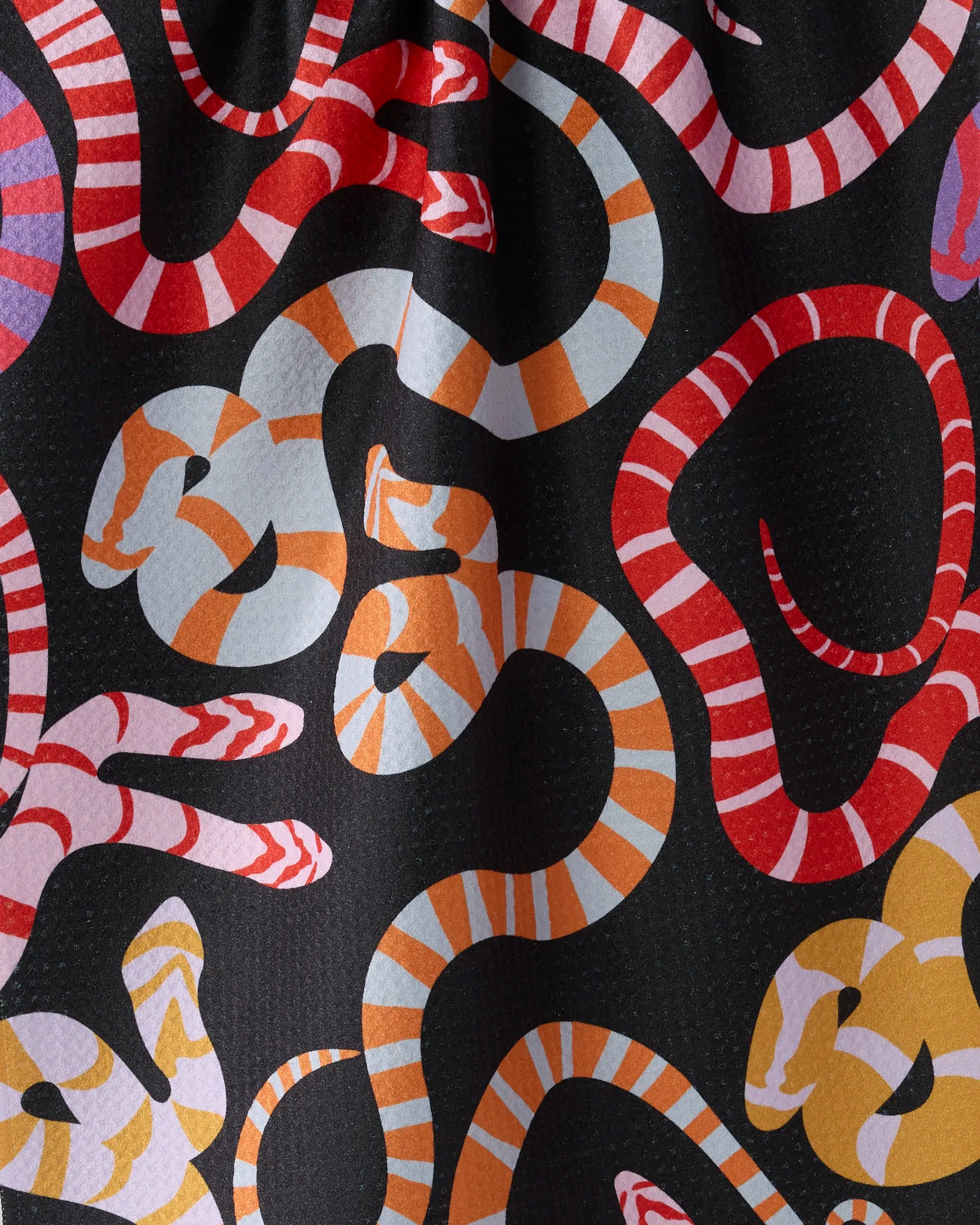 The Geometry Serpentine Riot kitchen towel, made from recycled materials, displays vibrant red, orange, pink, and yellow stylized snakes with striped and dotted patterns on a black background.