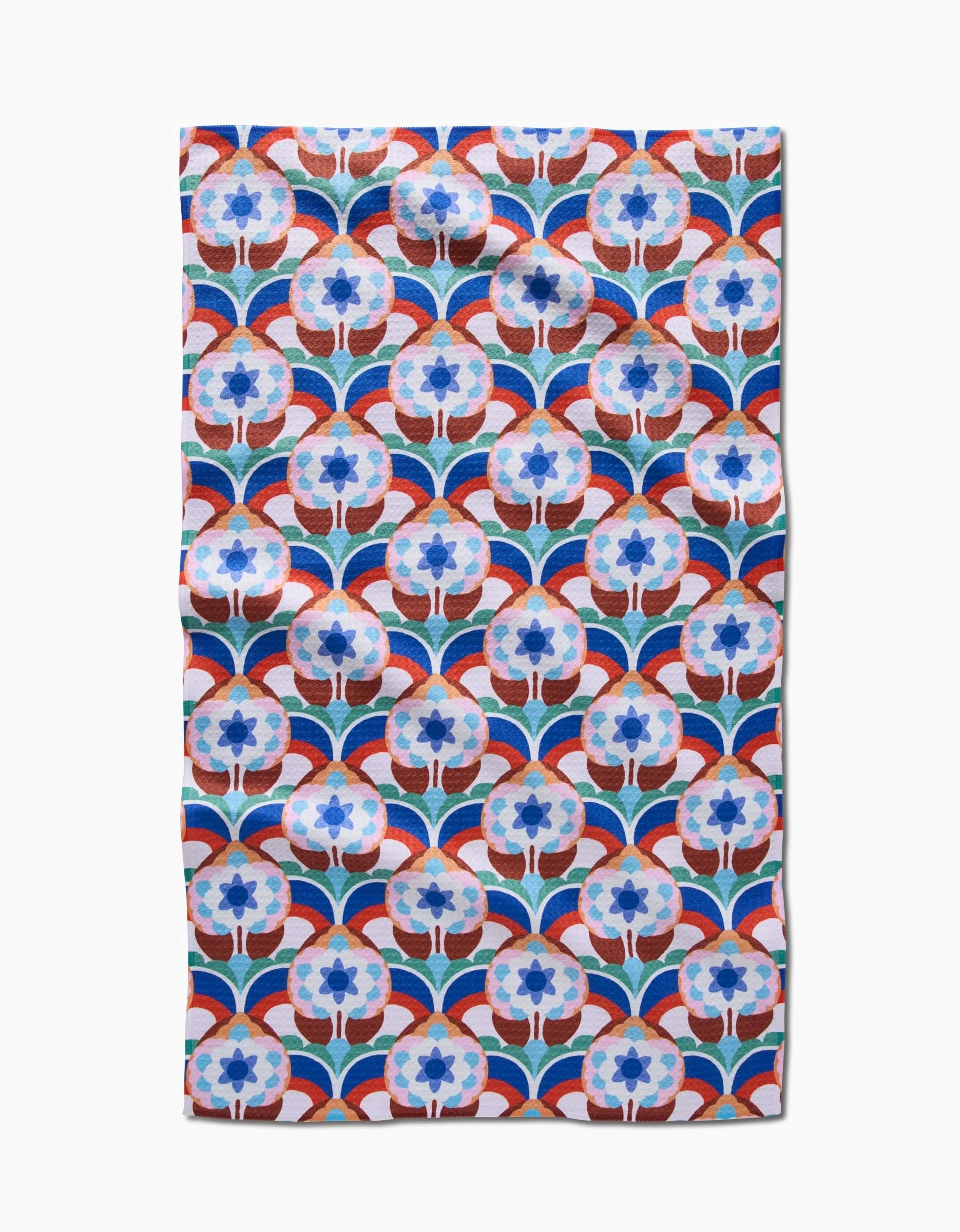 The Seventies Retro Flowers tea towel by Claire Iglesias features a blue and white floral pattern with red curved lines in a geometric retro style, made from recycled materials. Ultra-absorbent, slightly wrinkled fabric on a white background.