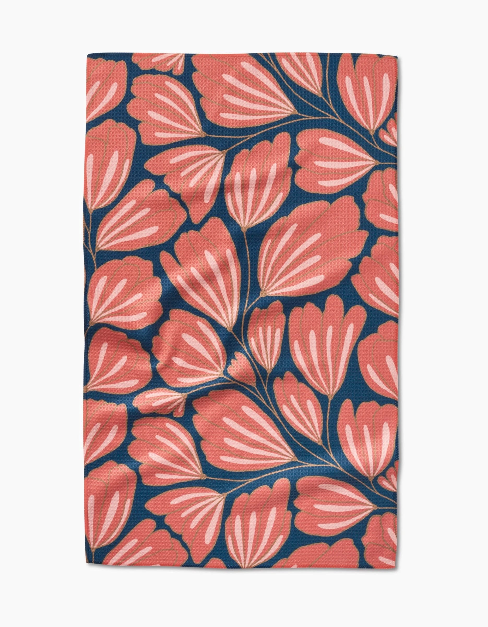 The Sheila tea towel by Amy MacCready showcases large stylized coral-pink leaves with white accents on dark blue, made from recycled materials and shown laid flat with slight wrinkles.
