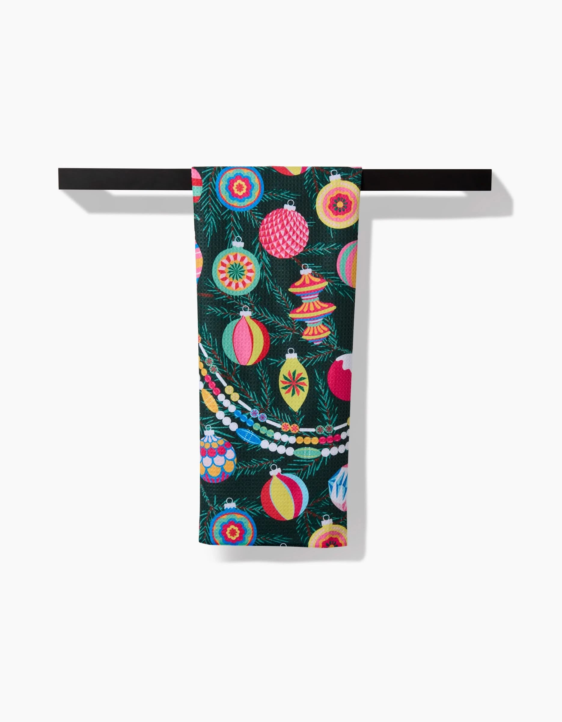 The Shiny Ornaments tea towel by Rebecca Bobko showcases colorful Christmas ornaments and garlands on dark green Geoweave fabric, draped over a black rod.