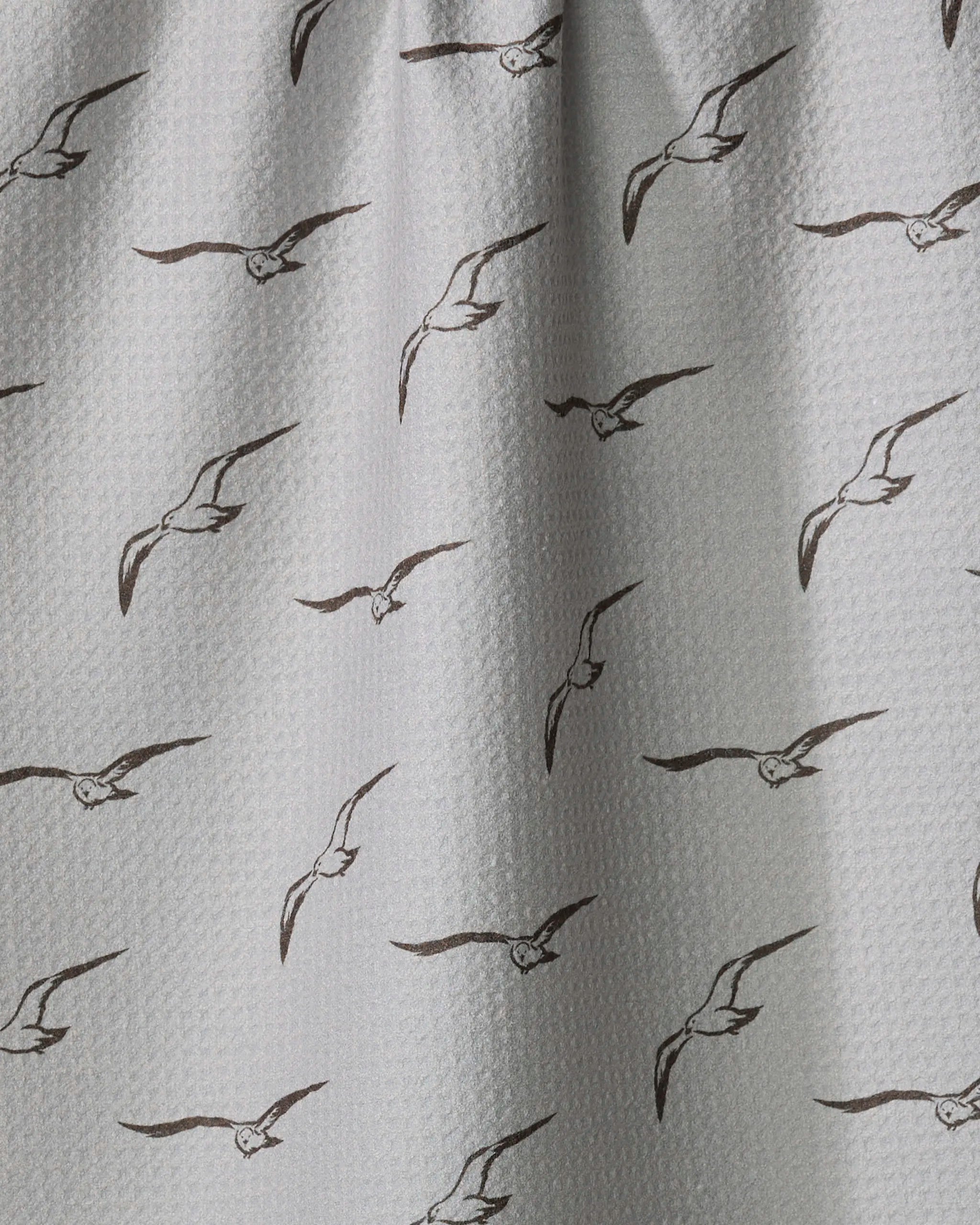 Shoreline Scout by Jenny Keller features white textured fabric with evenly spaced black line drawings of flying seagulls. Slightly gathered at the top, this charming tea towel adds a coastal touch to your kitchen.