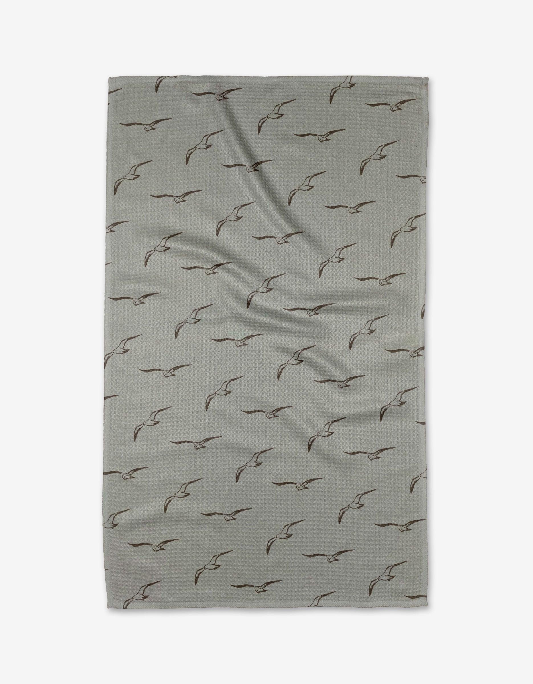 The Shoreline Scout by Jenny Keller is a light gray rectangular tea towel with black outlined flying birds in a diagonal pattern. Made from quick-drying recycled materials, it’s pictured flat with gentle creases.