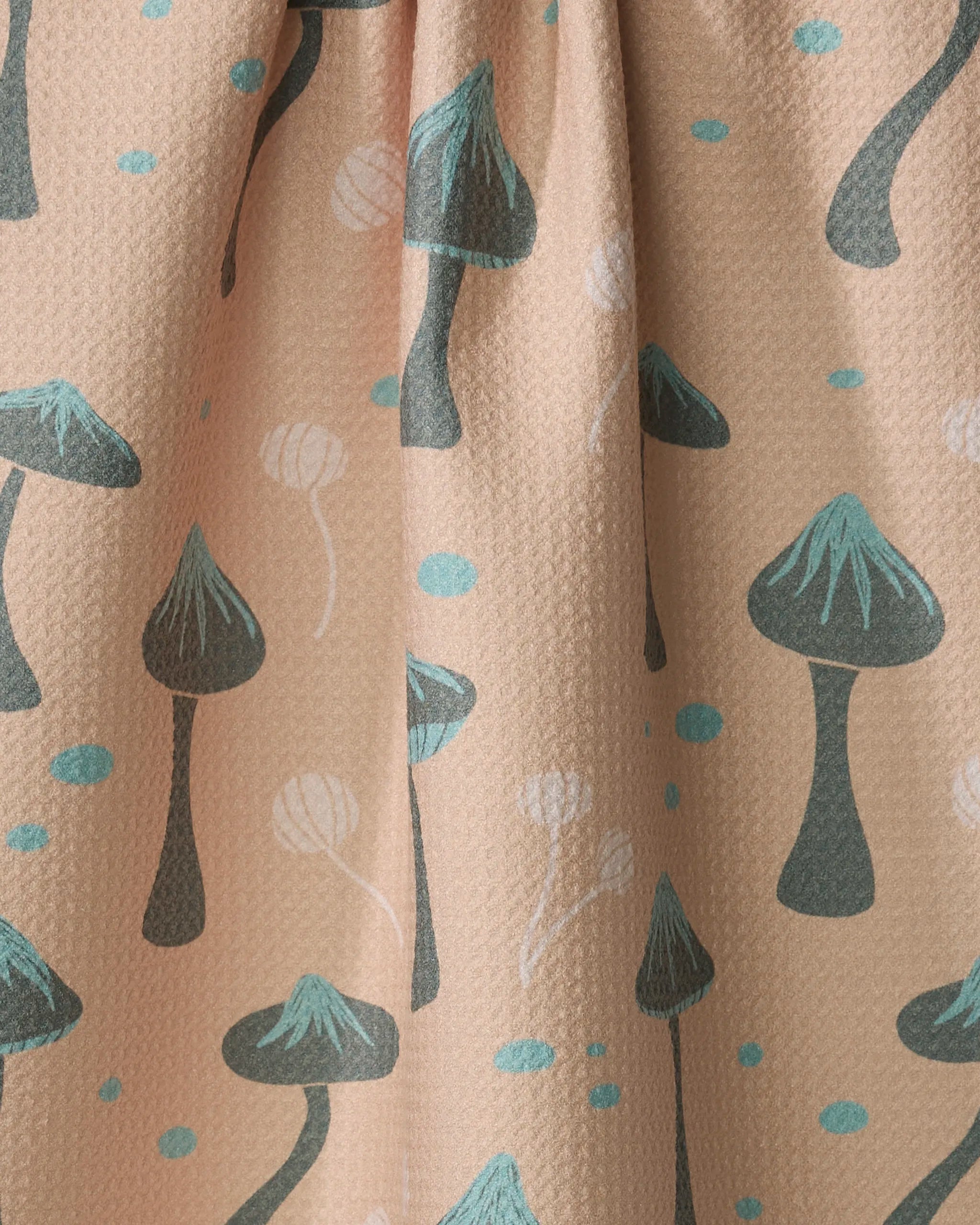 Close-up of the Shroom Sprouts recycled kitchen towel by Amberleigh Adoff against a beige background, featuring stylized teal and black mushrooms, small teal dots, white lines, and a textured, slightly wrinkled fabric.