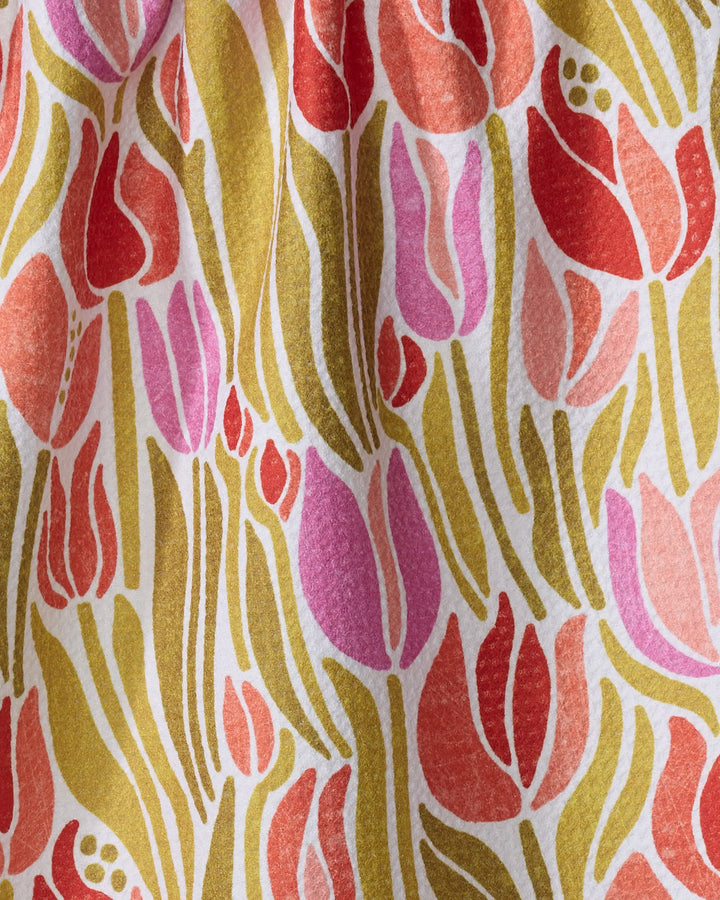 The Sidney towel by Amy MacCready features a colorful, abstract tulip design in red, pink, purple, and olive green on white textured fabric. Elongated tulip shapes and leaves create a closely arranged, repeating pattern. Ultra-absorbent.