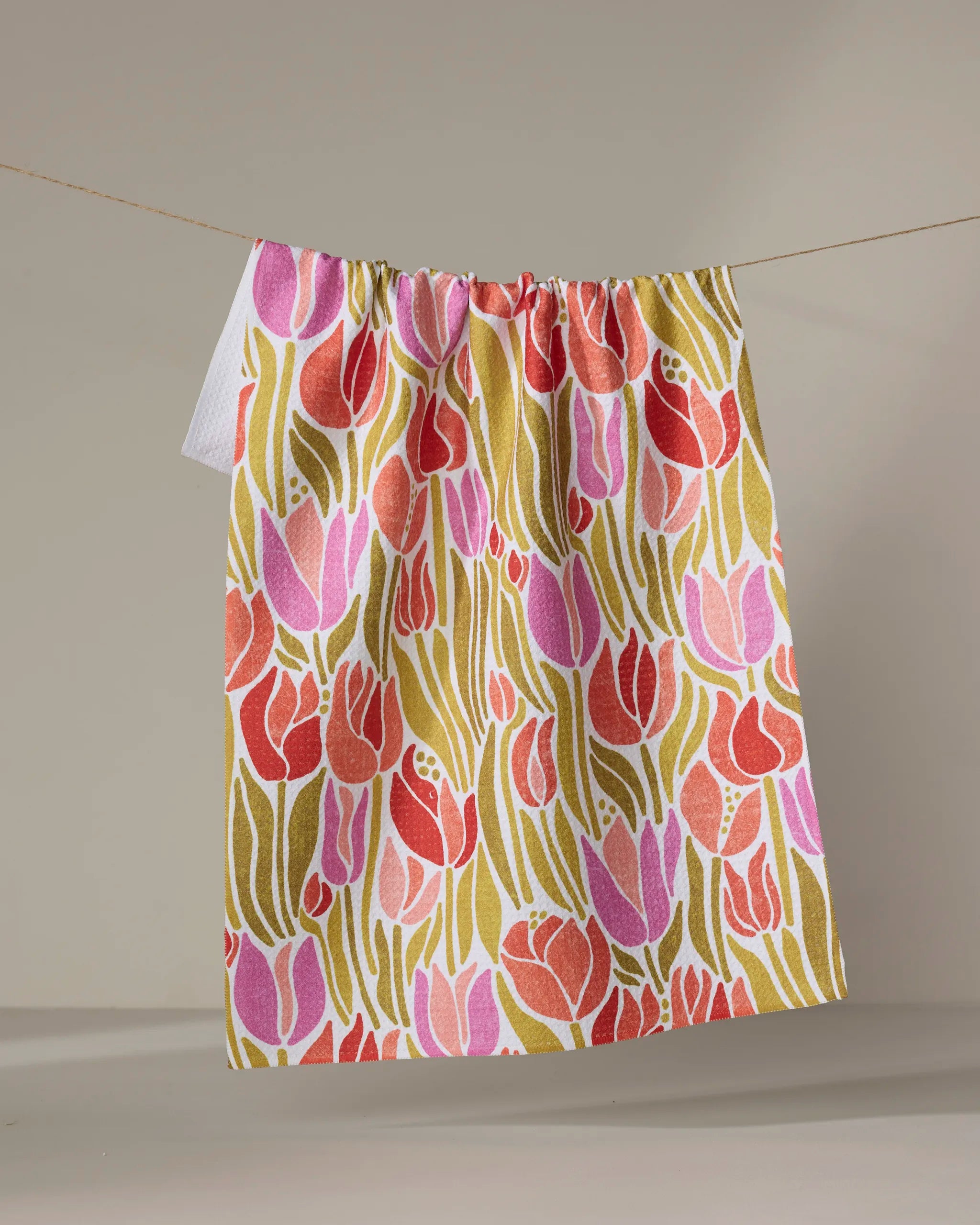 The Sidney towel by Amy MacCready, featuring a vibrant tulip and green leaf pattern, hangs ultra-absorbent on a clothesline against a neutral backdrop.