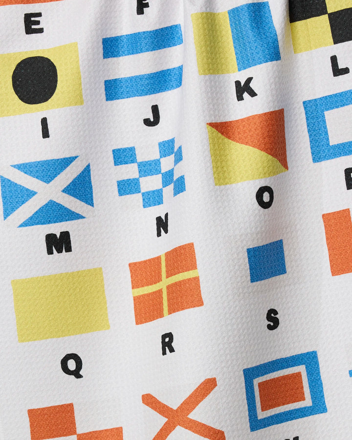 The Signal Flags kitchen towel by Geometry is made from recycled materials and features a white background with colorful nautical flag prints, each marked with a black-letter alphabet.