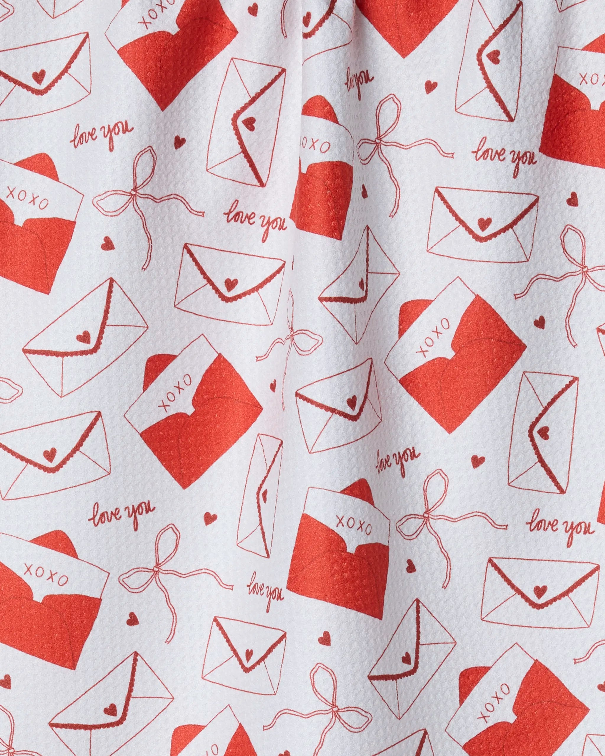 The "Signed" tea towel by Geometry features a red pattern of envelopes, hearts, bows, and loving phrases on white fabric—a romantic Valentine’s Day touch. Made from ultra-absorbent recycled materials for daily use.