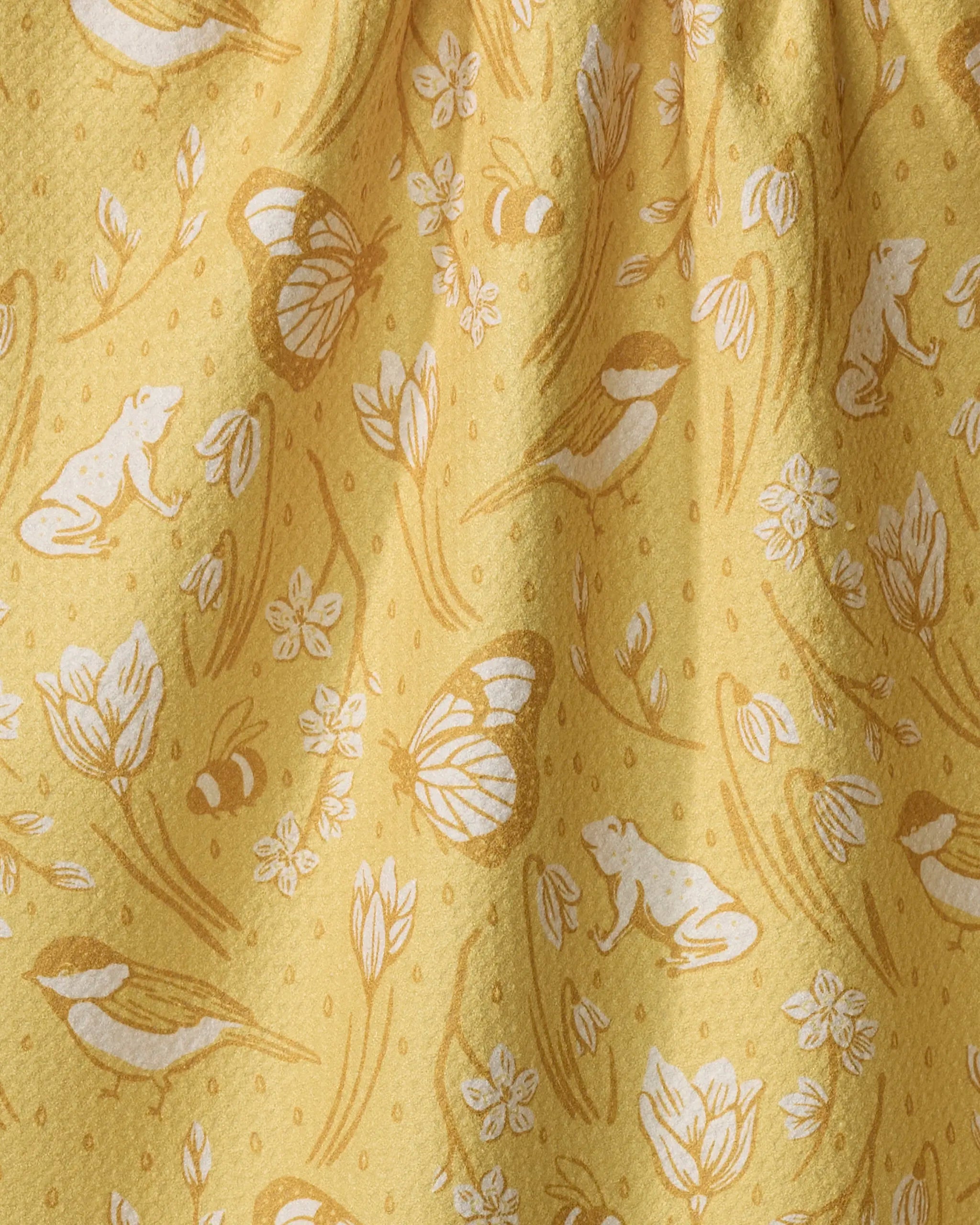 Signs of Spring" by Sarah Daugherty is a yellow recycled kitchen towel with a white and gold nature-themed pattern—frogs, bees, butterflies, birds, flowers, and leaves—and features gathered fabric for gentle folds and shadows.