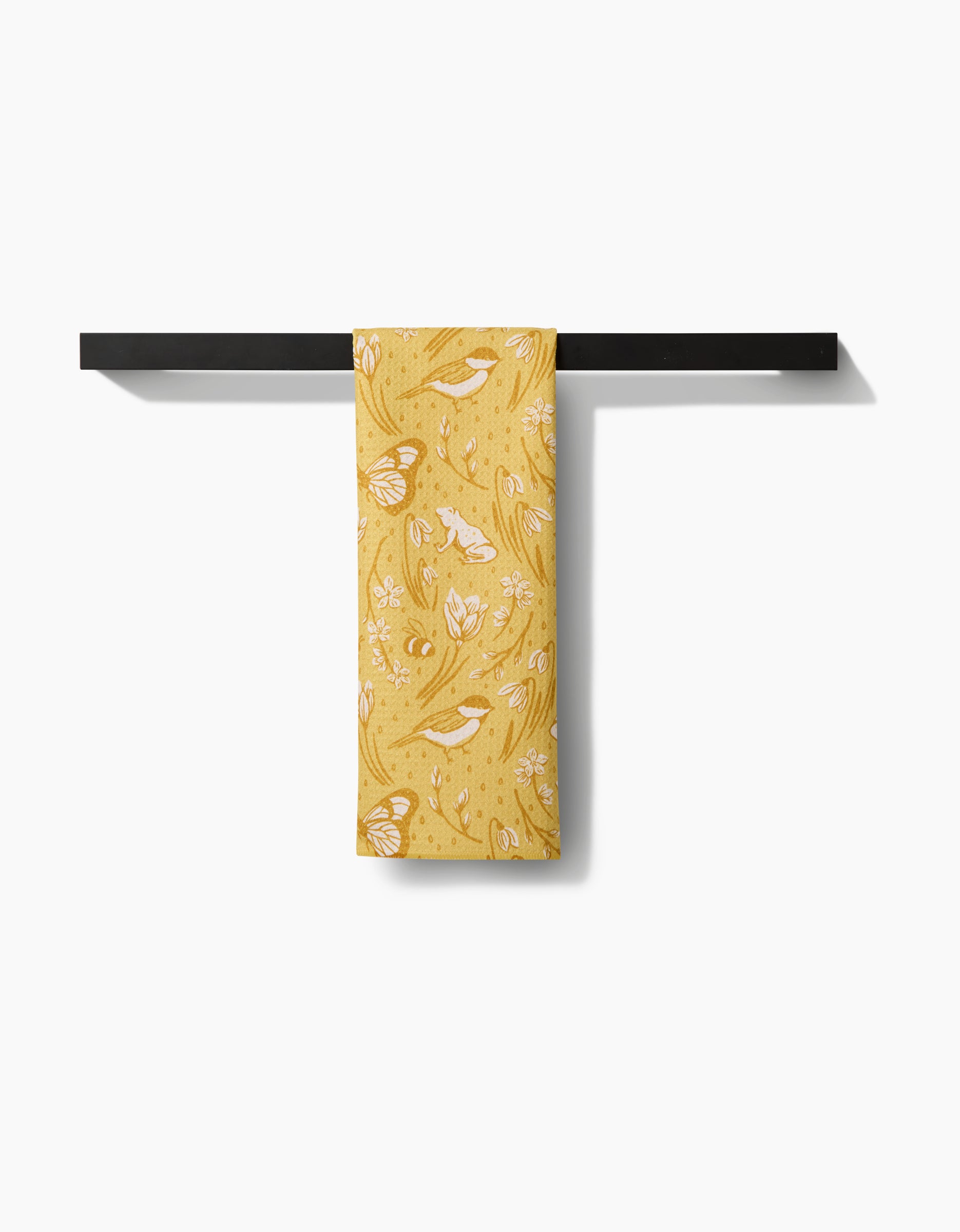 A yellow floral-patterned Signs of Spring tea towel by Sarah Daugherty, crafted from ultra-absorbent Geoweave fabric, hangs neatly on a sleek black towel bar against a plain white background.