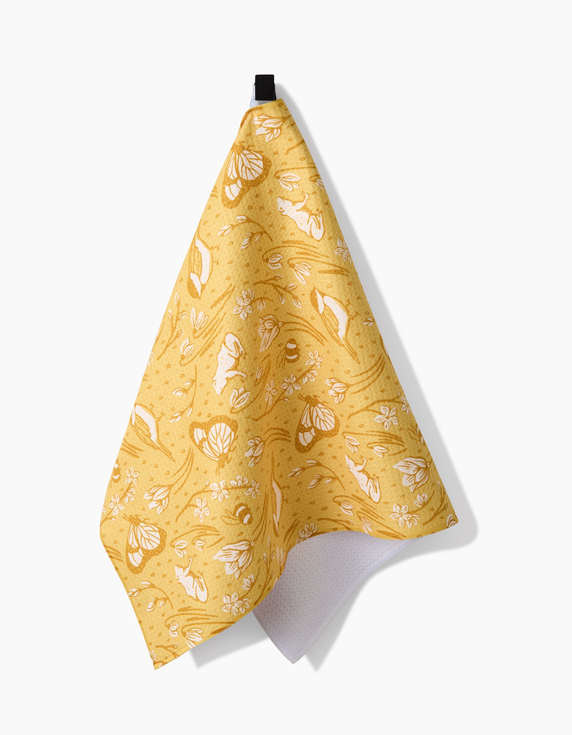 The Signs of Spring tea towel by Sarah Daugherty features white floral and butterfly patterns on yellow Geoweave fabric, with a textured ultra-absorbent white underside visible, hanging from a black loop against a plain background.