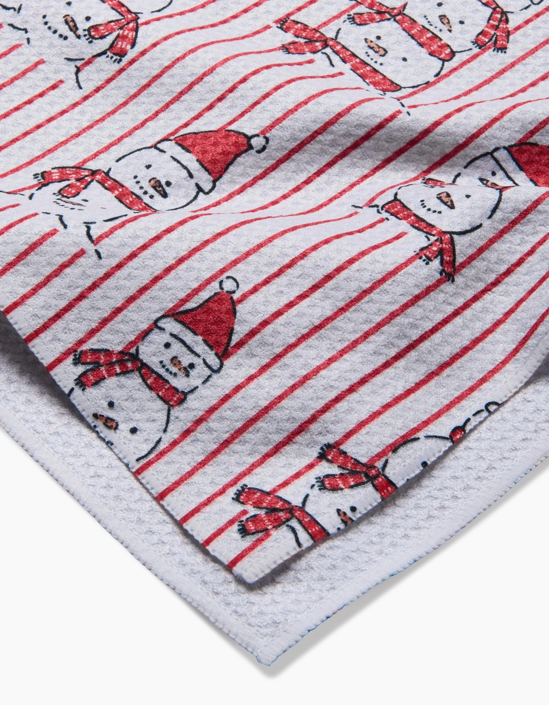 Close-up of the Hufton Studio Silly Snowman kitchen towel, made from recycled materials, with red and white stripes and snowmen in red hats and scarves on a white textured background.