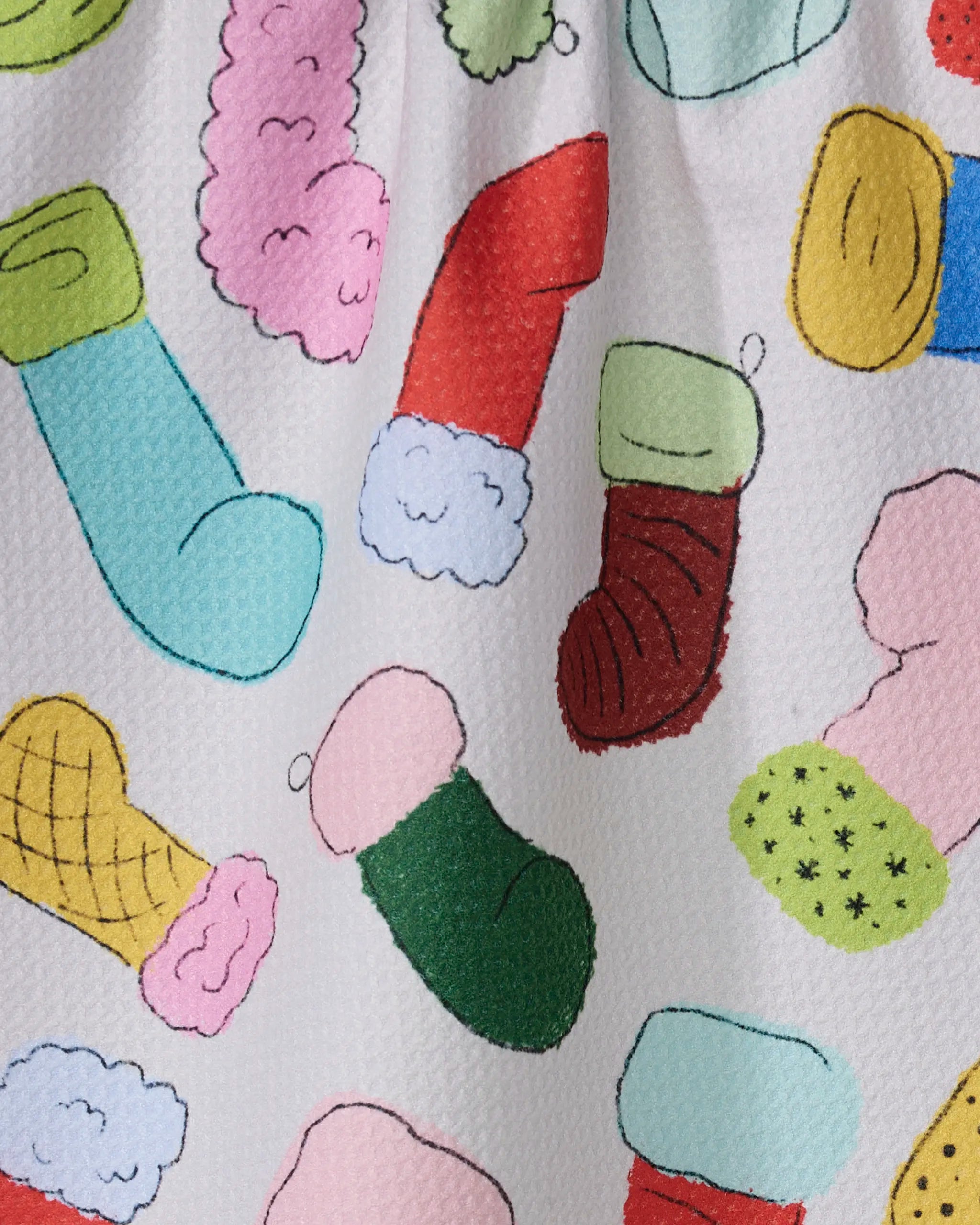 Geometry’s Silly Stockings tea towel features a playful pattern of colorful, hand-drawn Christmas stockings and mittens on a white textured background, creating an ultra-absorbent and festive addition to your kitchen.