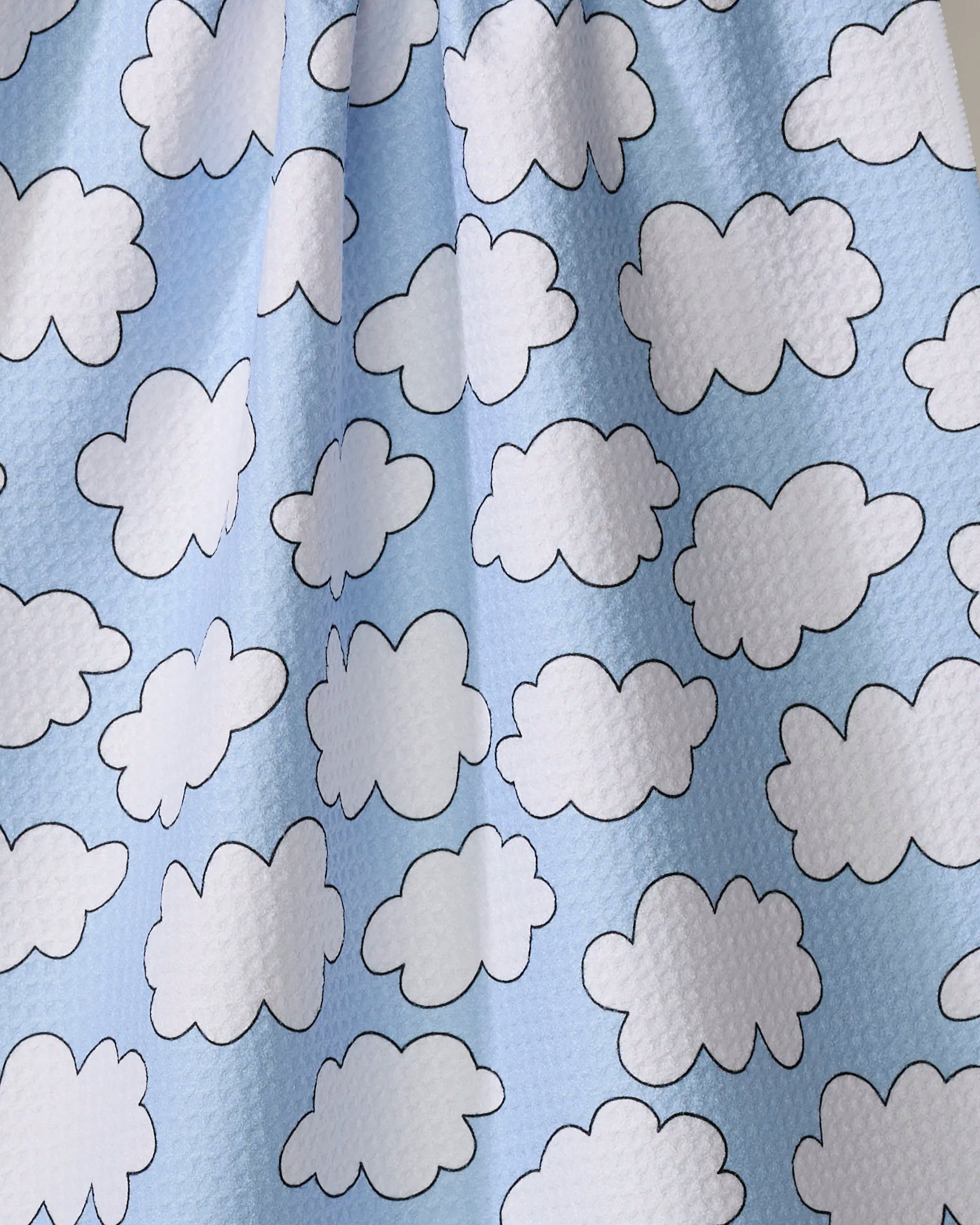 The Silver Linings tea towel by Mindfulnice is made from recycled materials and features a light blue background with a repeating pattern of white, black-outlined cartoon clouds.