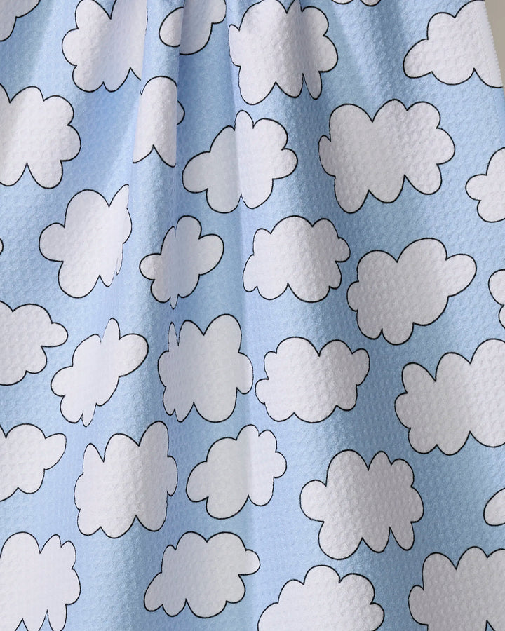 The Silver Linings tea towel by Mindfulnice is made from recycled materials and features a light blue background with a repeating pattern of white, black-outlined cartoon clouds.