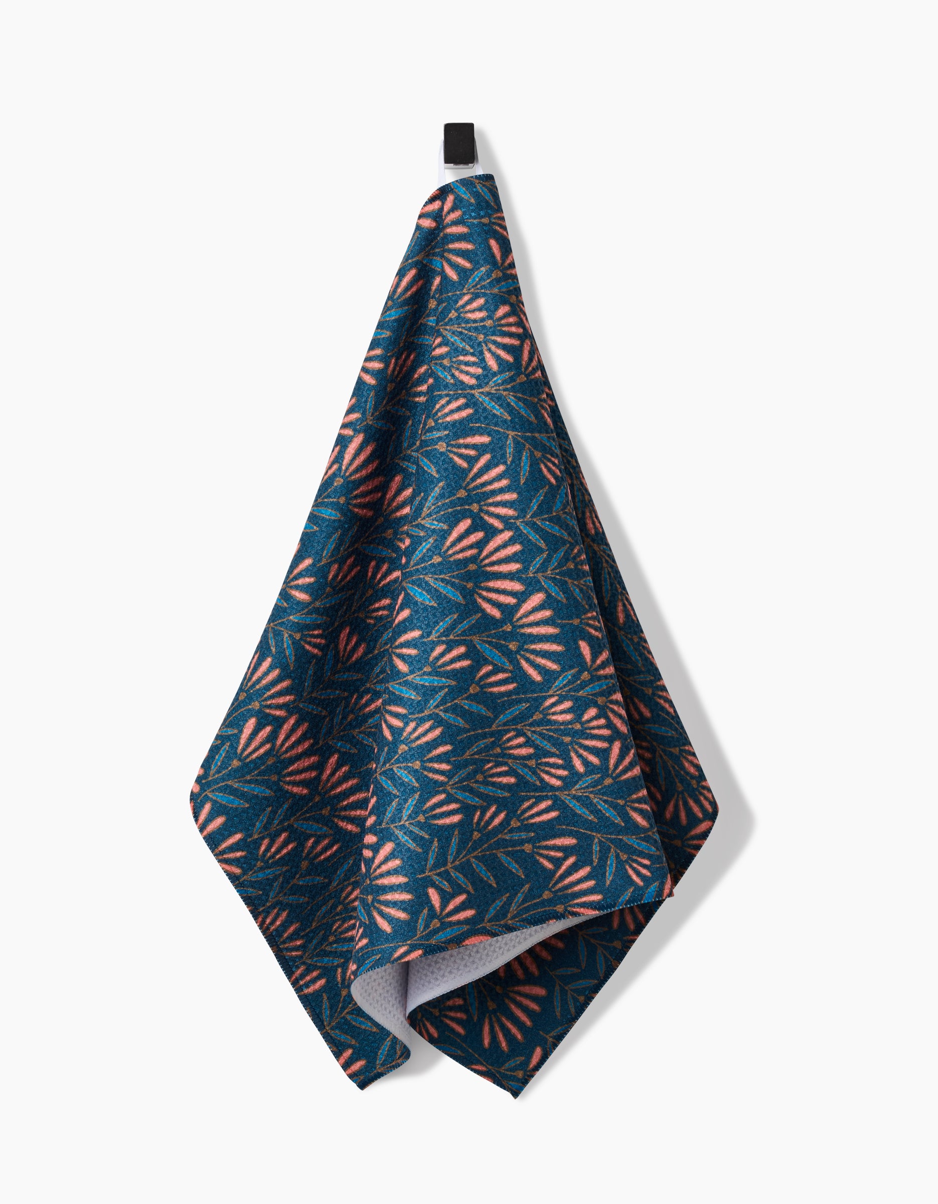 The Sirocco tea towel by Amy MacCready features a blue, ultra-absorbent design with a pink and white geometric leaf pattern, hanging from a black loop against a white background.