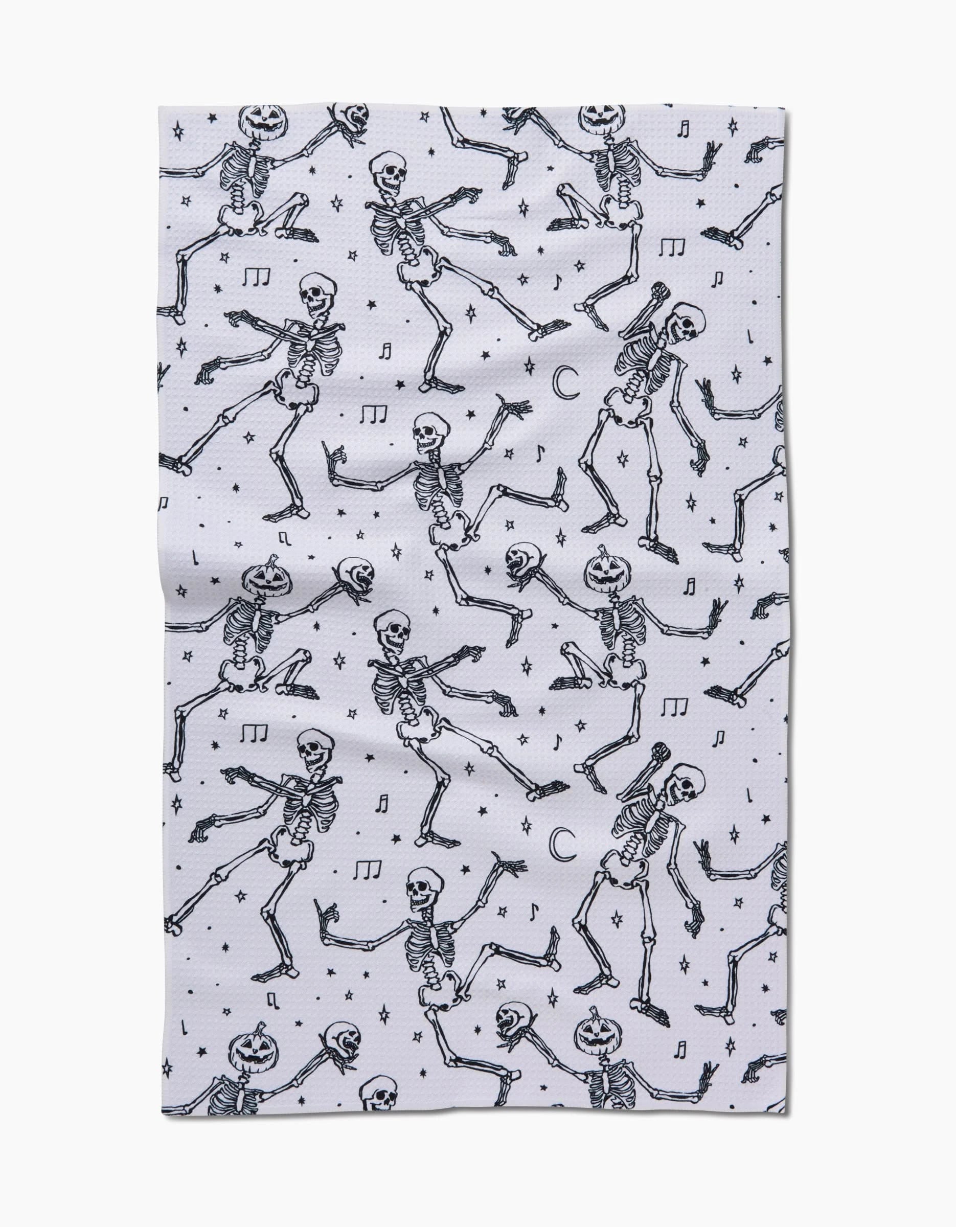 The Skeleton Halloween Dance tea towel by Aubrey Fairchild features playful black skeletons, musical notes, stars, and crescent moons on white Geoweave fabric—a unique and high-quality kitchen essential.