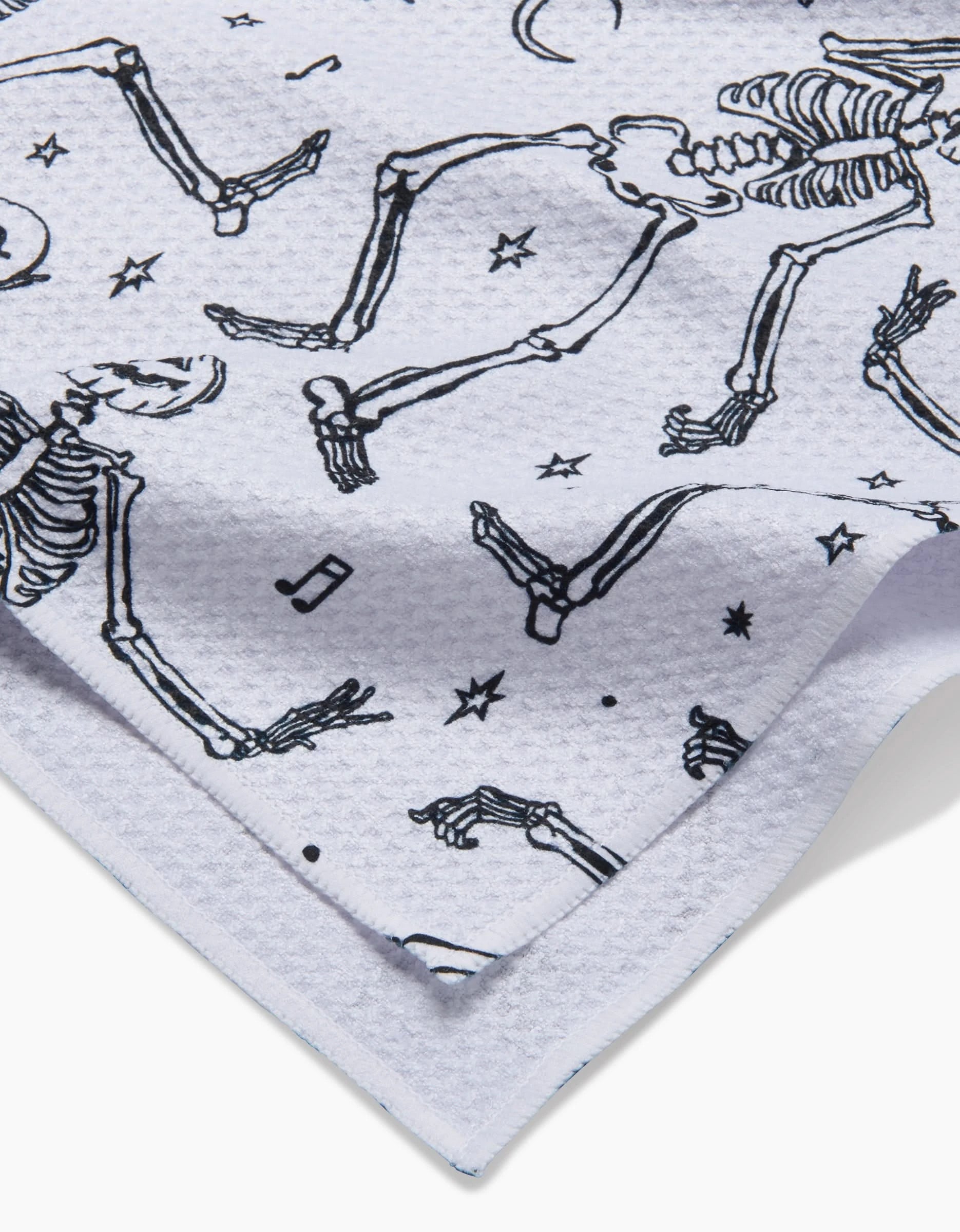 Aubrey Fairchild’s Skeleton Halloween Dance tea towel features a white textured Geoweave fabric with a black print of dancing skeletons, musical notes, stars, and crescent moons.