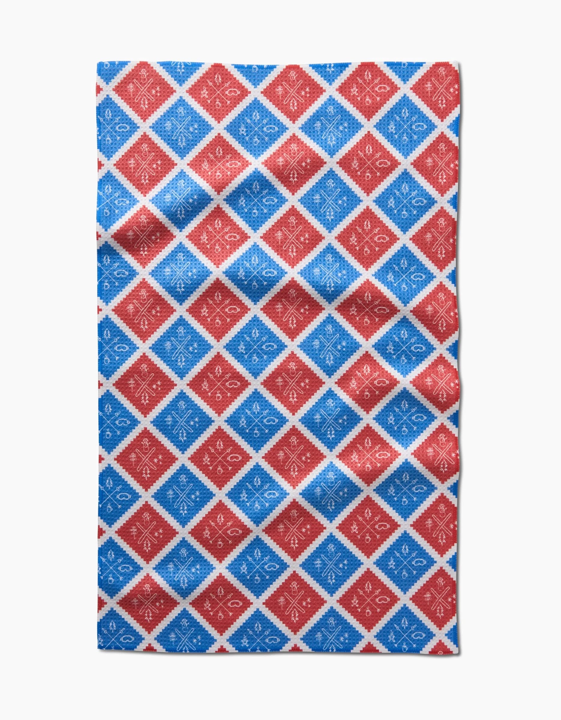 The Rosa Kichline Ski Patch tea towel displays a rectangular design with red and blue diamond patterns, each featuring small white snowflake or star motifs arranged in an orderly, alternating grid.