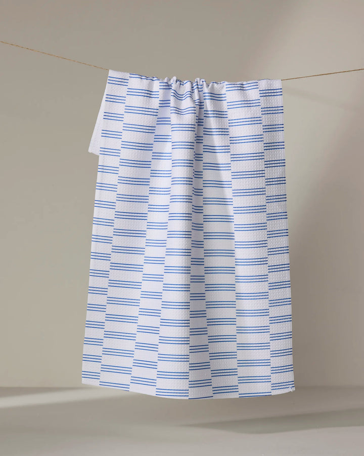 The Buy Guide’s Small Stripe - Navy tea towel, featuring absorbent white fabric with evenly spaced navy stripes, hangs from a string against a neutral background.