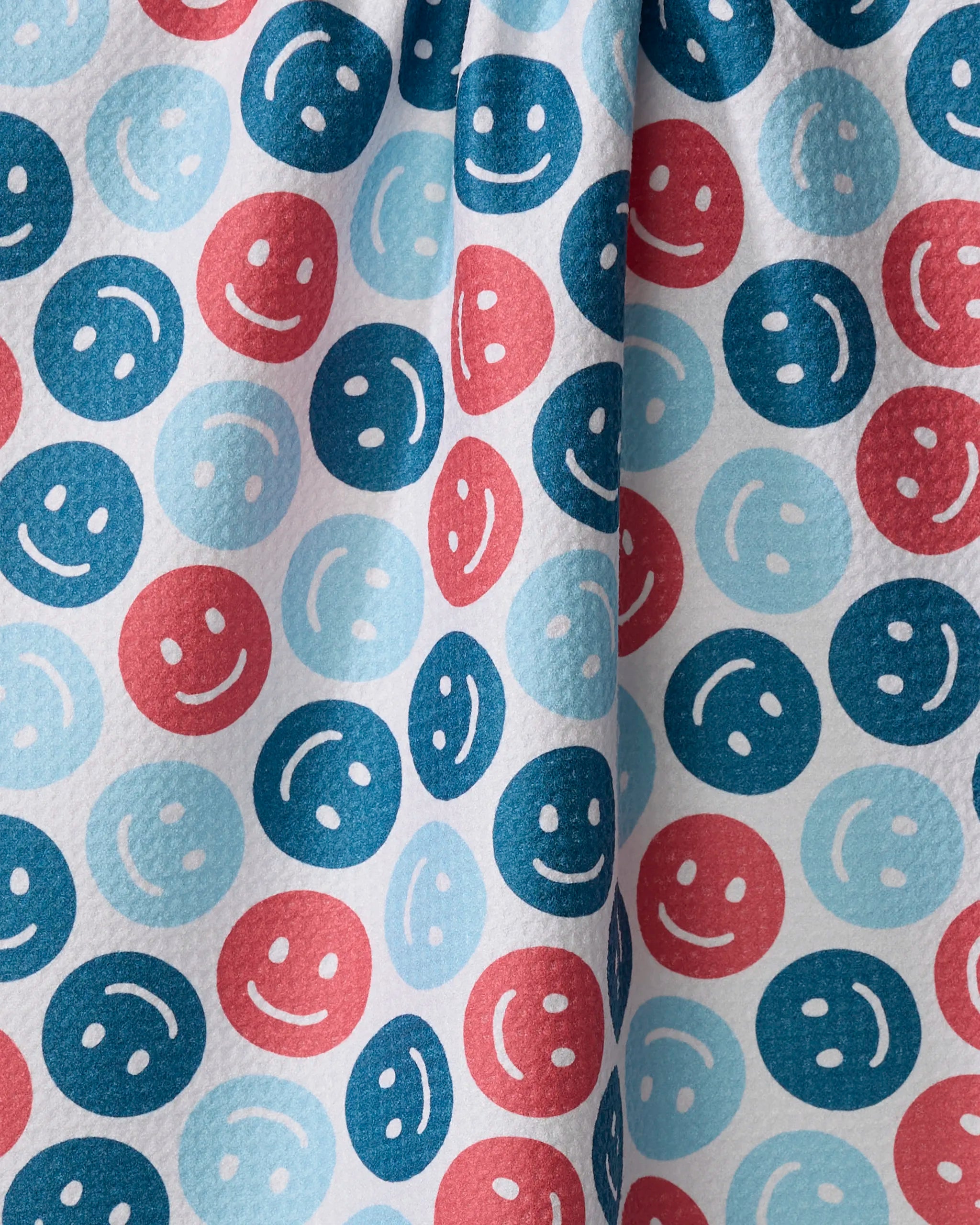 Smiley Face July by Hufton Studio is a recycled fabric with blue, red, and light blue smiley faces on white. Its slightly gathered texture makes it ideal for a playful kitchen or tea towel.