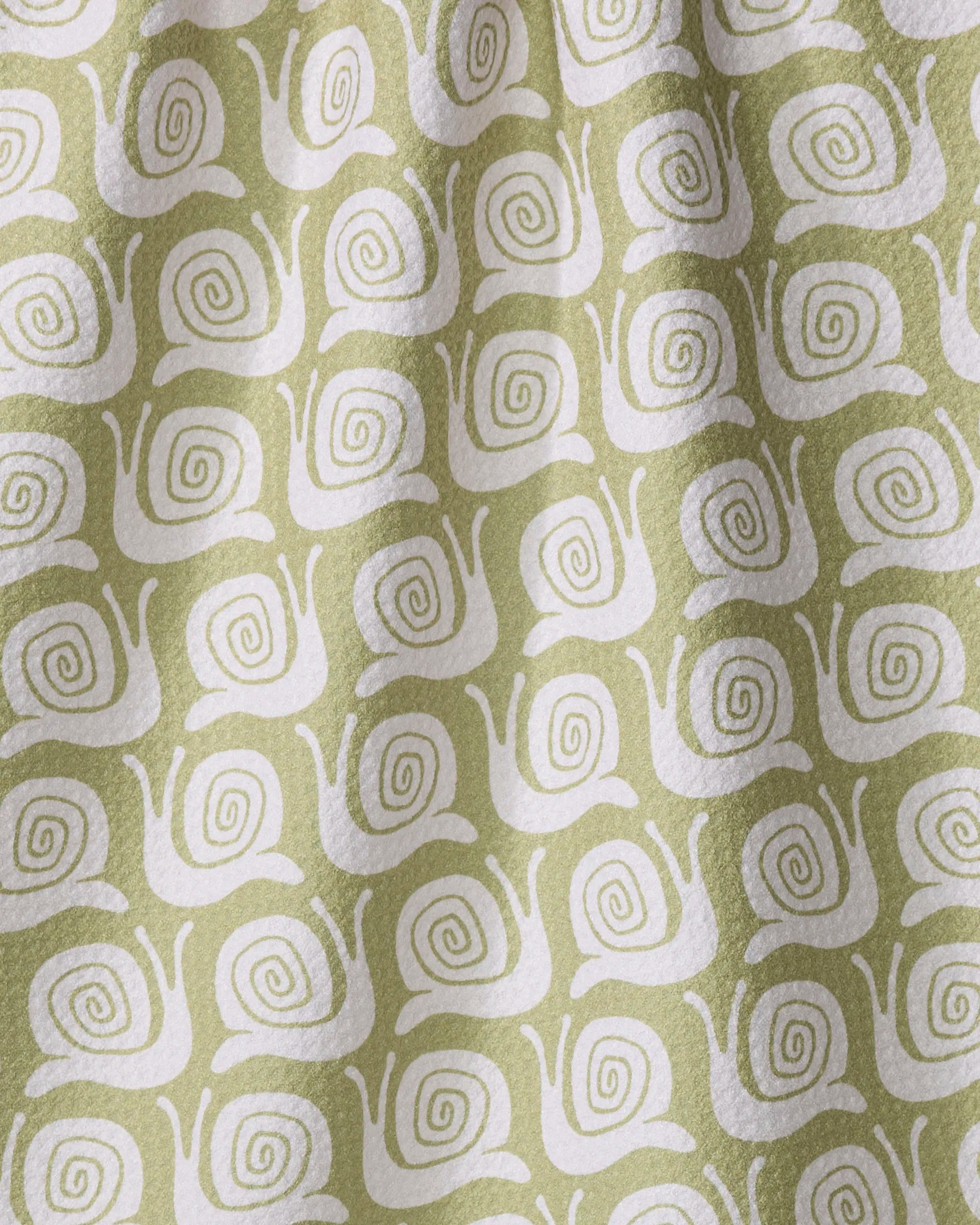 The Snail Party kitchen towel by Kayla Ann features a repeating pattern of white, stylized snails with spiral shells on green fabric made from recycled materials. Gentle folds and shadows are visible on the eco-friendly towel.
