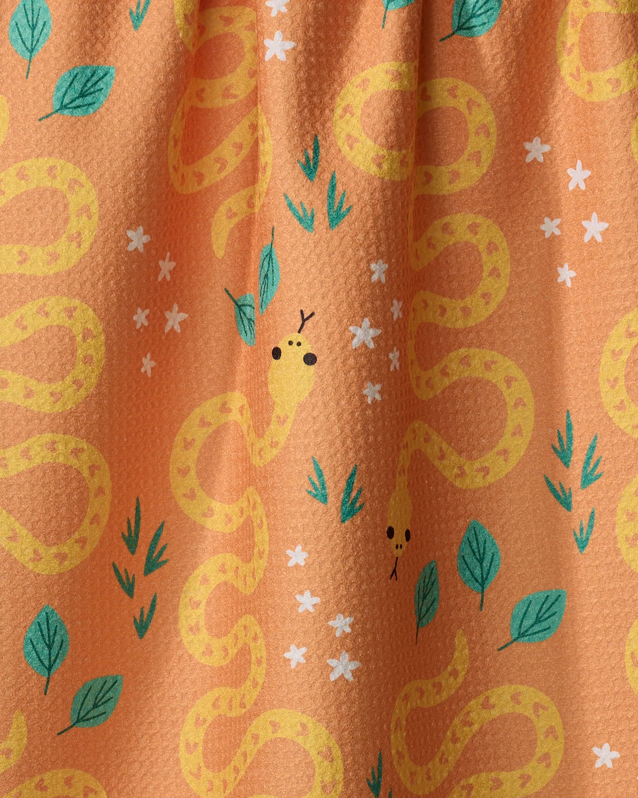 The Genna Blackburn "Snakes" tea towel features a playful orange design with yellow cartoon snakes, green leaves, and white flowers. Made from recycled materials, its ultra-absorbent textured surface shows friendly snake faces.